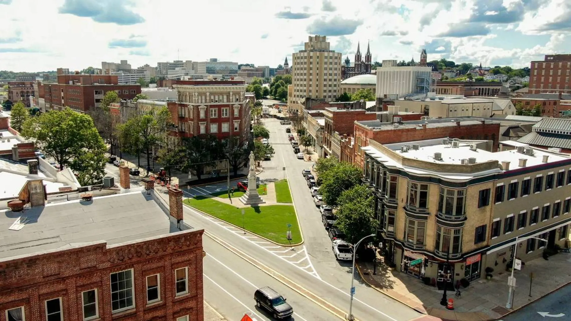 Aerial view of a downtown street with historic brick buildings, green park, and a cloudy sky.