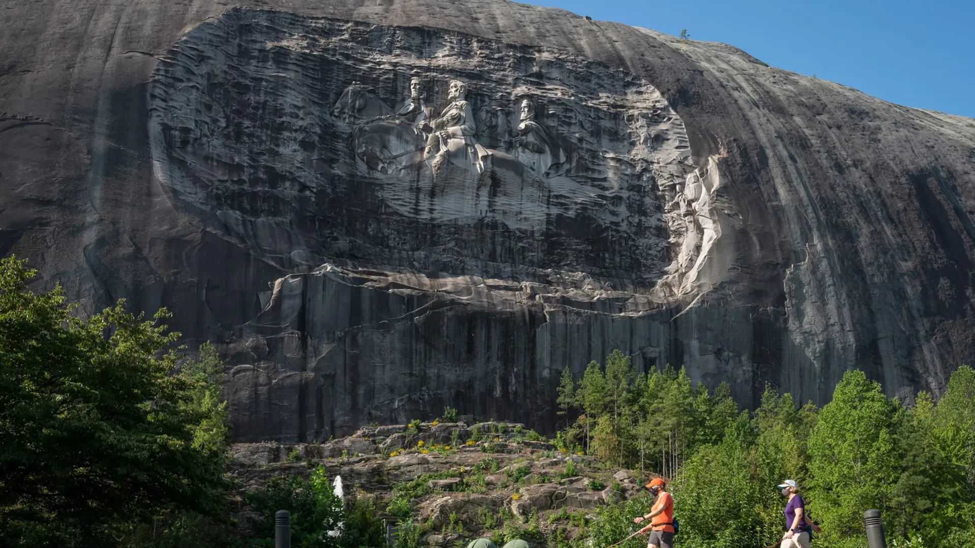 People walking dogs in front of Stone Mountain with Confederate Memorial carving under clear blue sky