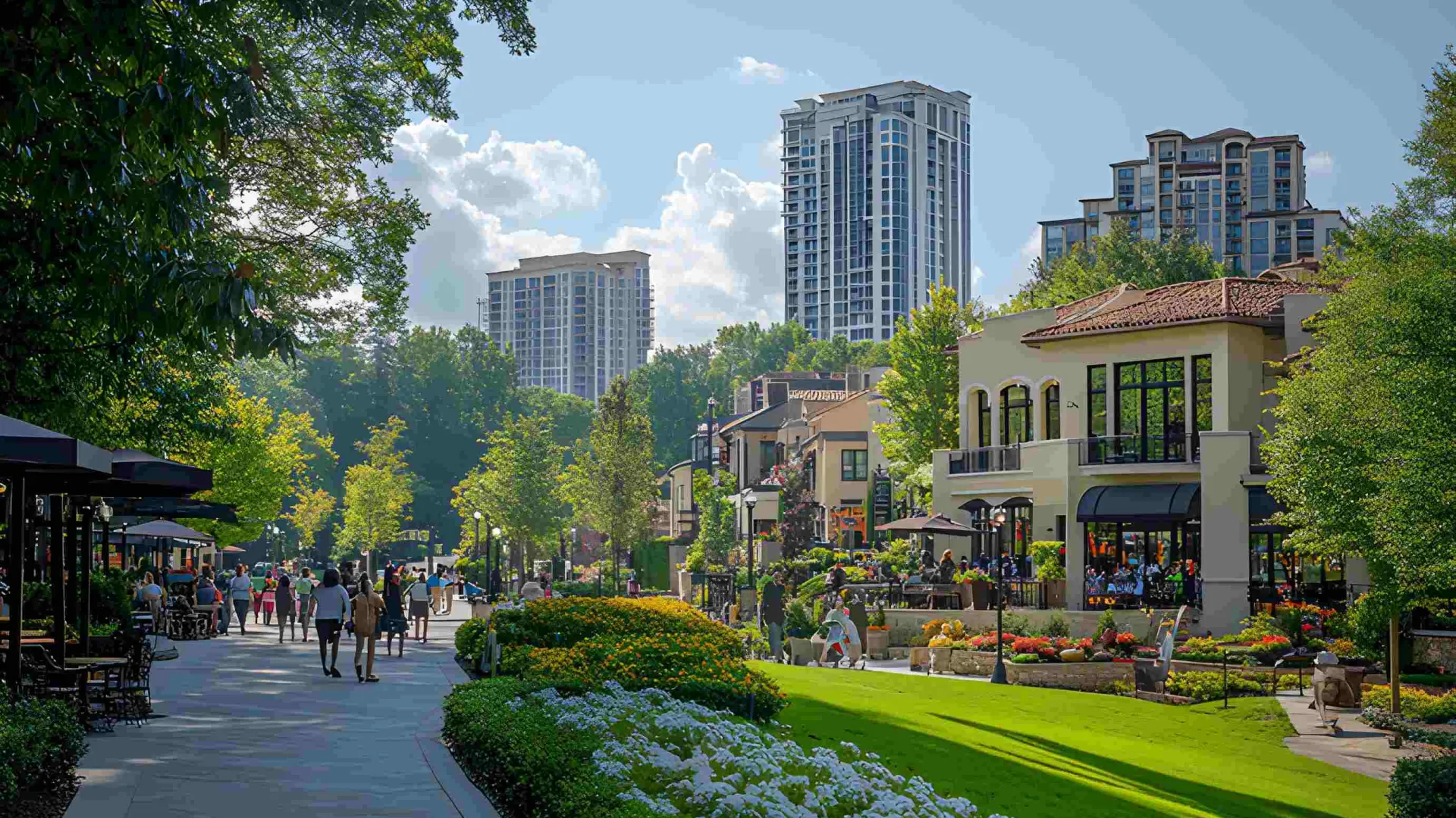 Urban pedestrian street with greenery, modern shops, people walking, and tall buildings under a clear sky.