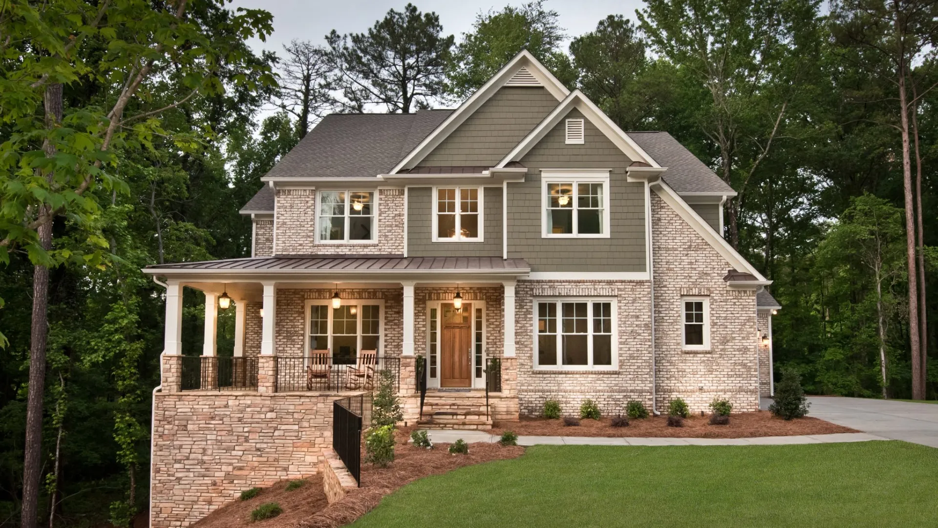 Two-story suburban house with brick and siding exterior, front porch, and well-maintained lawn surrounded by trees