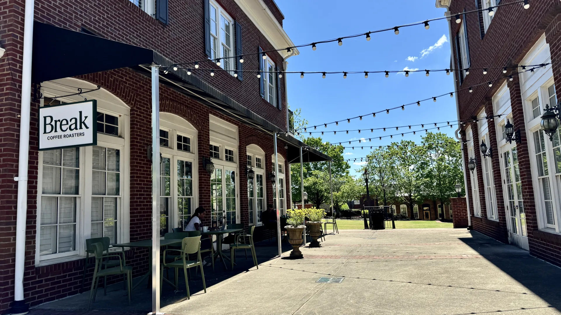Outdoor seating area of Break Coffee Roasters with brick buildings, string lights, and clear blue sky on a sunny day.