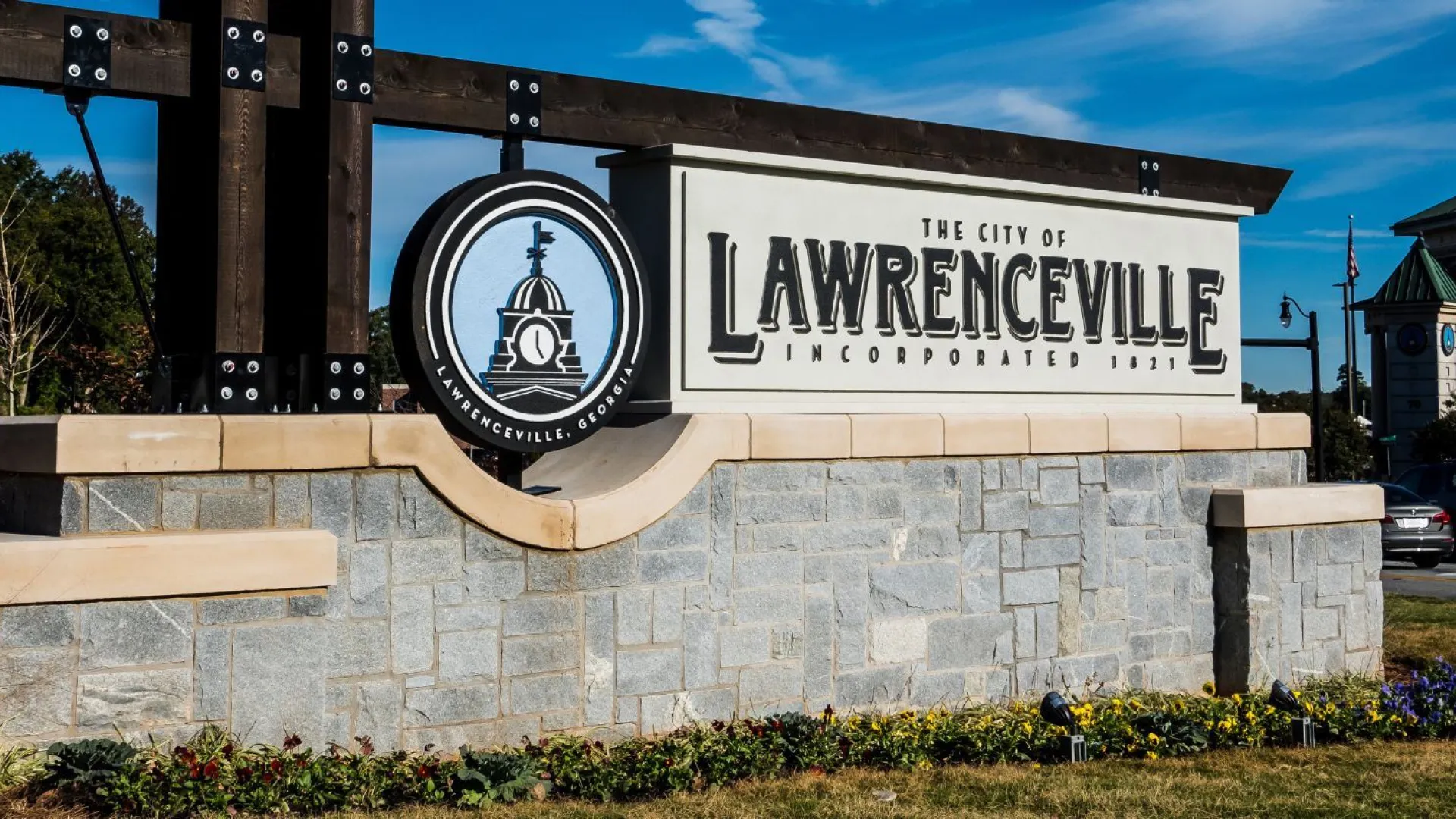 Welcome sign for the City of Lawrenceville on a stone base with clear blue sky and nearby buildings in the background