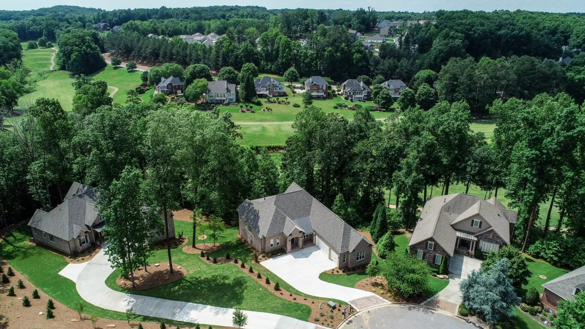 Aerial view of suburban houses surrounded by trees with a golf course and more homes in the background