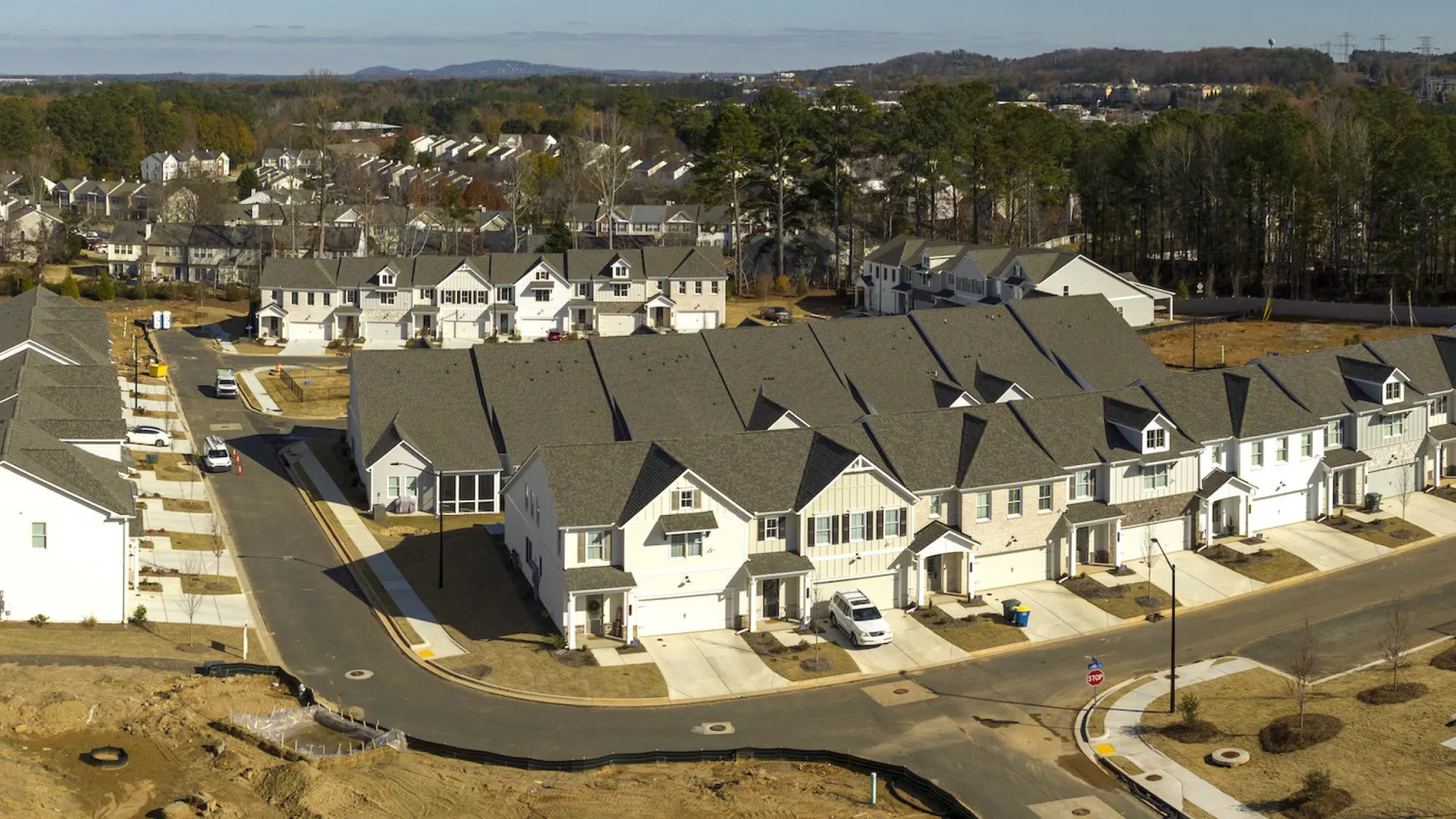 Aerial view of a suburban neighborhood with newly built townhouses and surrounding greenery under clear skies.