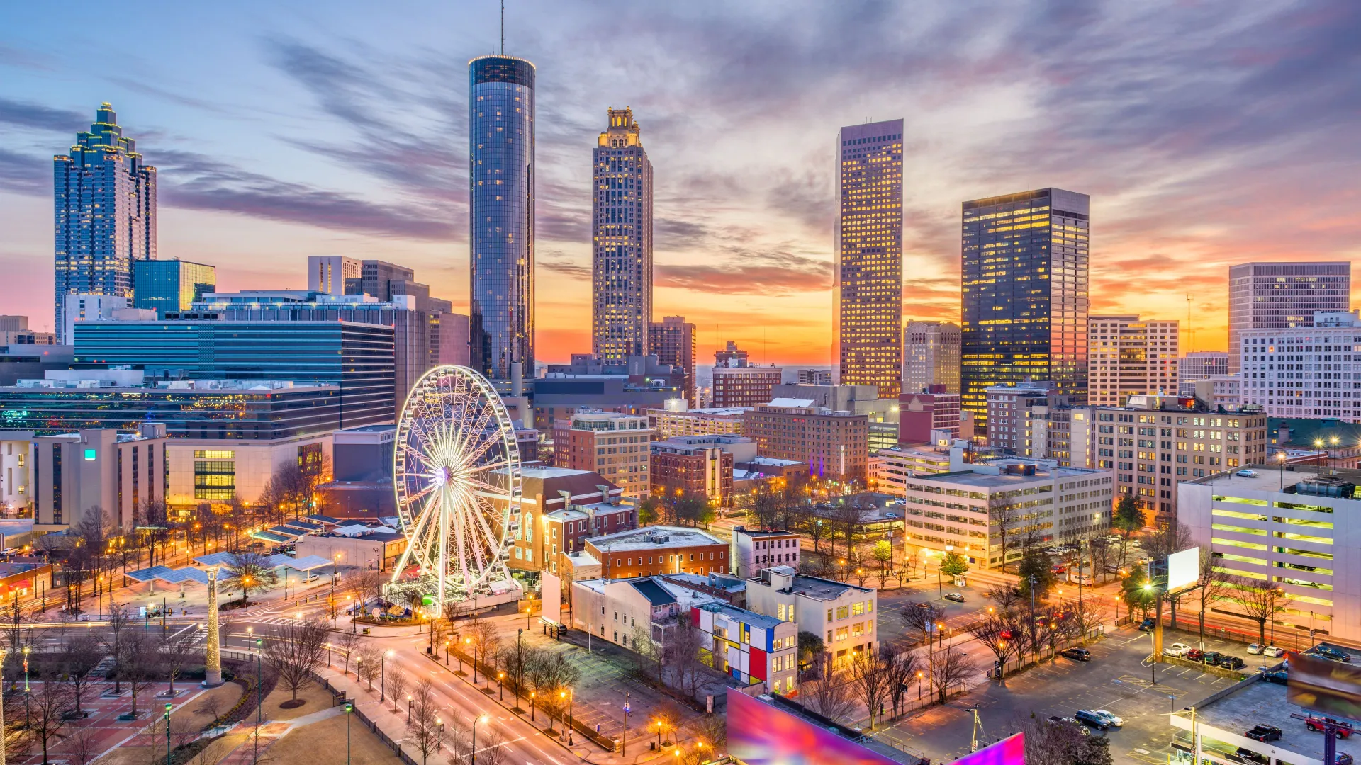 Atlanta city skyline at sunset with illuminated Ferris wheel and tall buildings under colorful sky