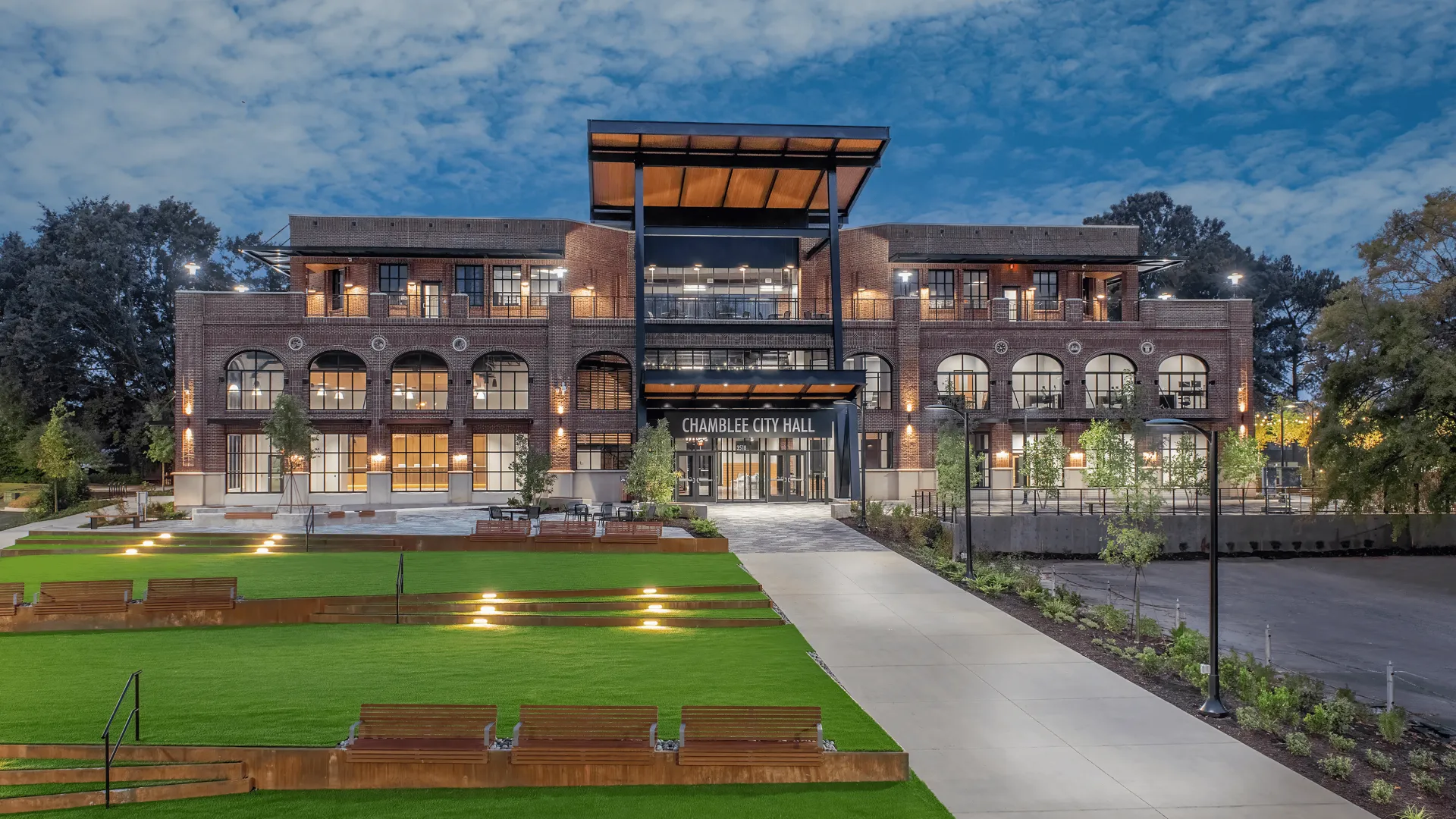 Chamblee City Hall building with illuminated windows and landscaped green lawn under a cloudy evening sky