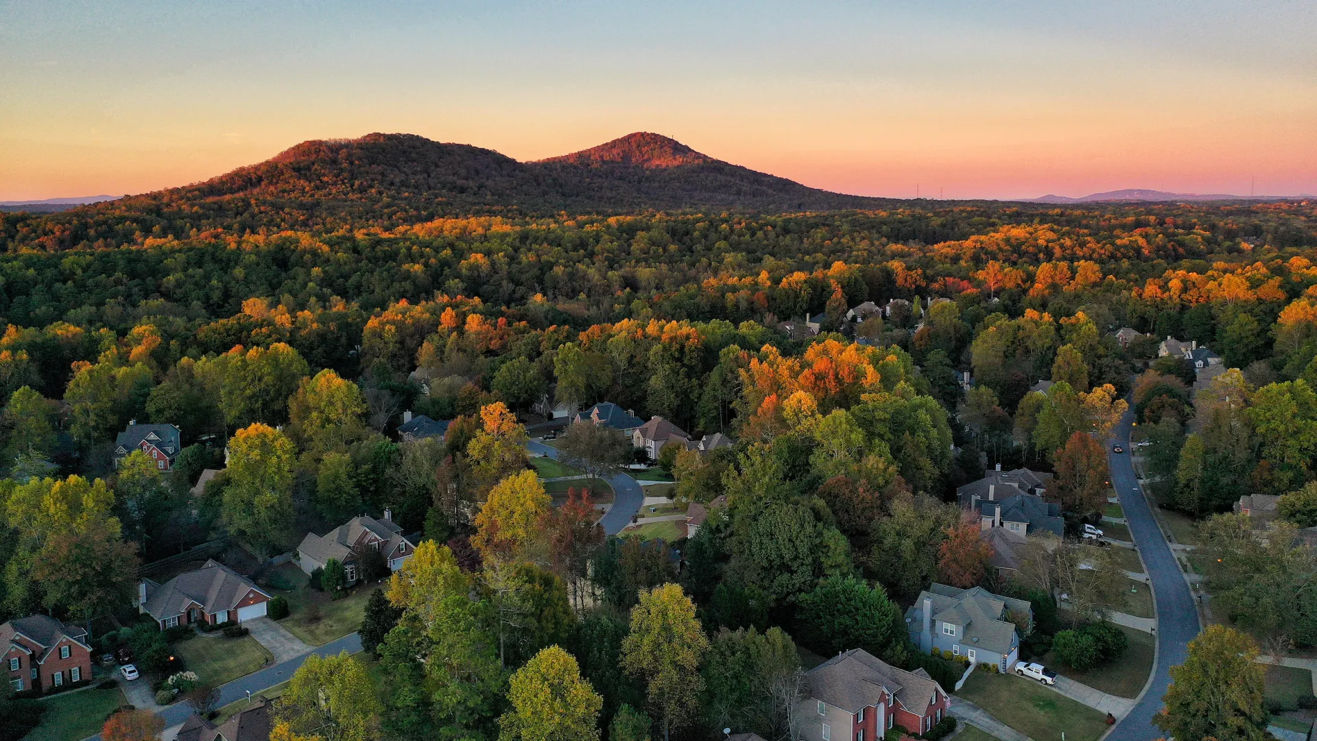 Aerial view of a suburban neighborhood in Kennesaw GA with fall foliage and rolling hills at sunset under a clear sky