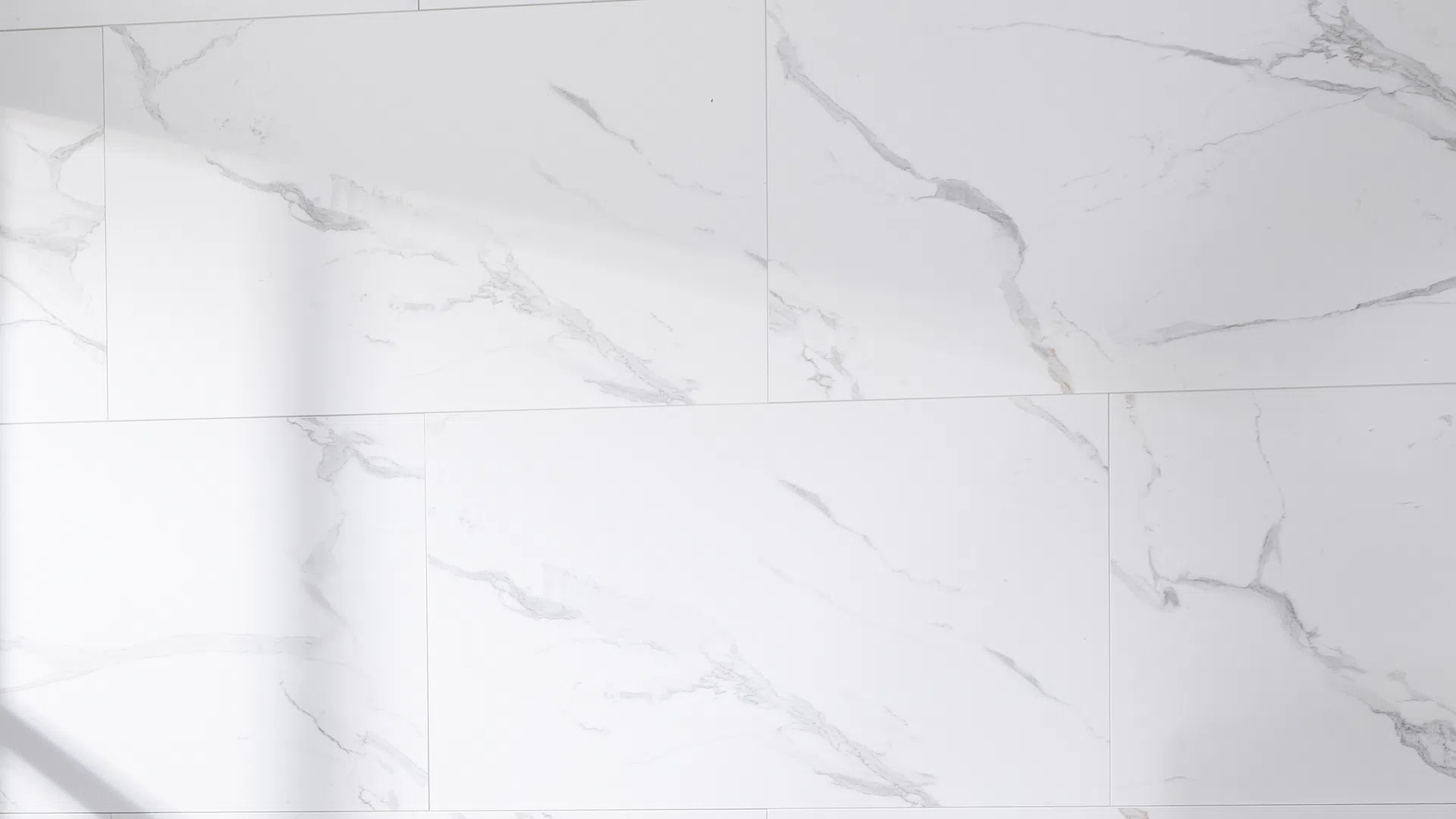 White marble tiles with gray veining arranged in a staggered pattern on a smooth surface.