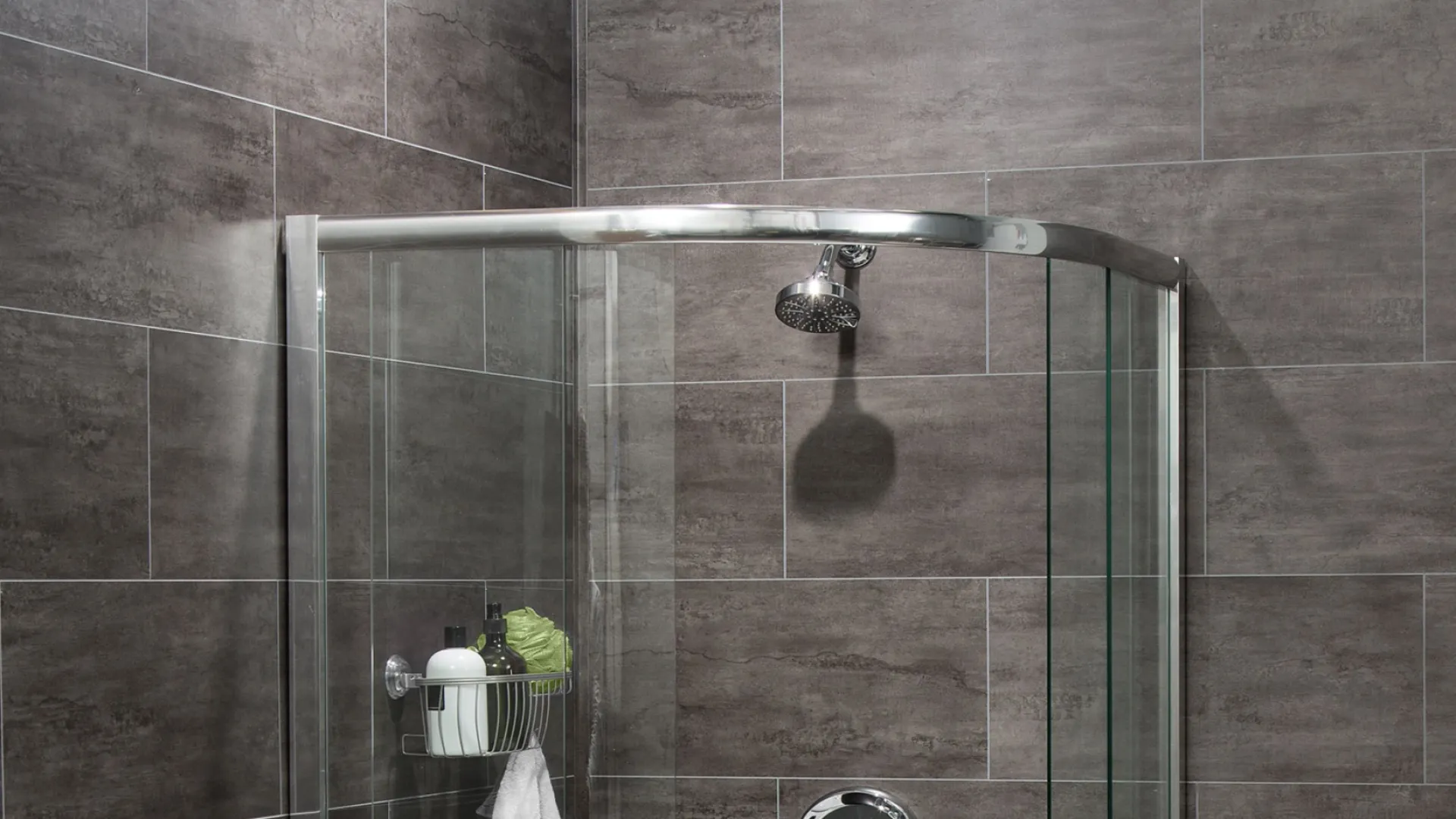 Modern shower with curved glass door and dark gray tiled walls in a bathroom.