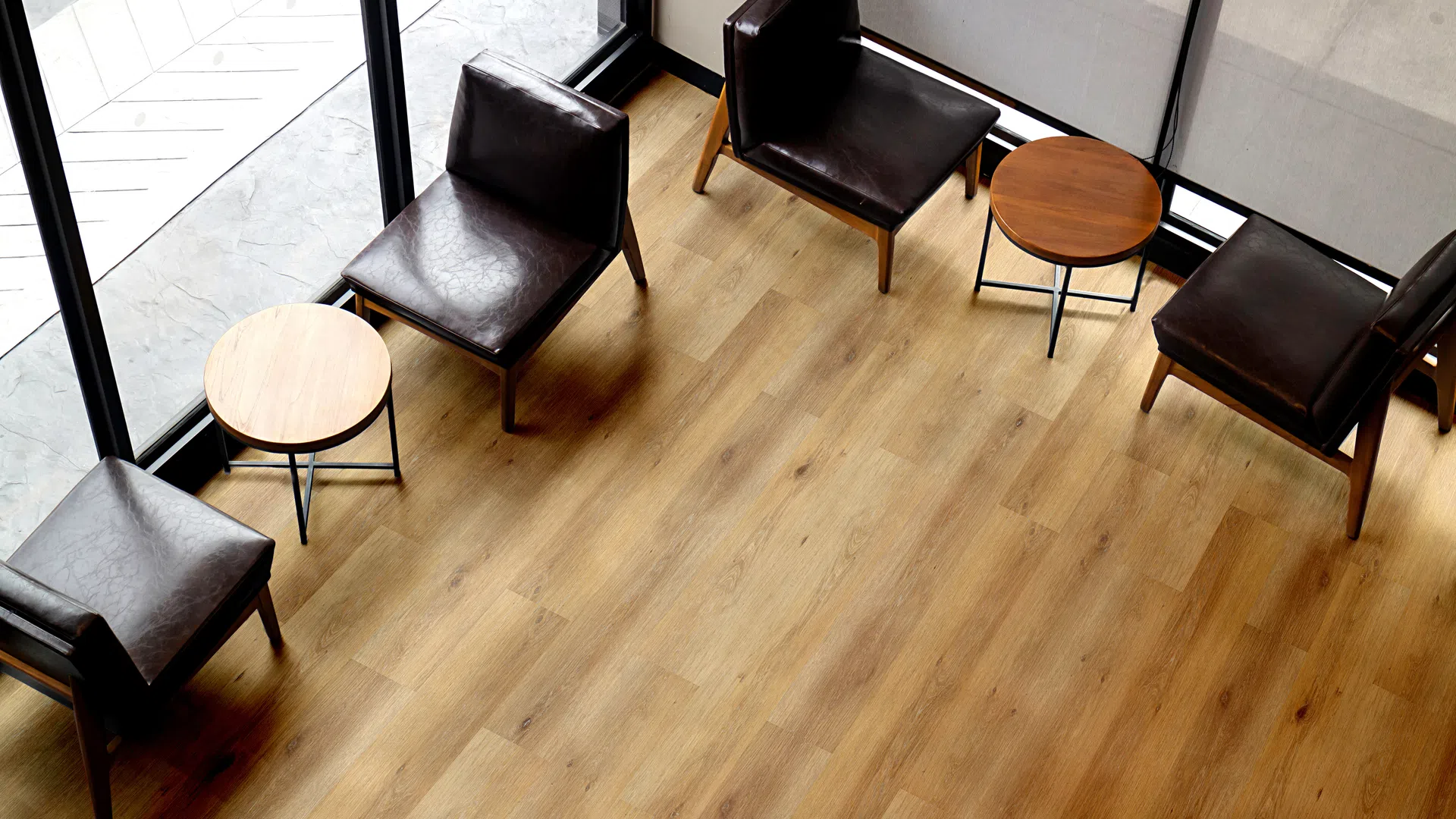 Minimalist seating area with black leather chairs and wooden round tables on light hardwood floor near large windows.