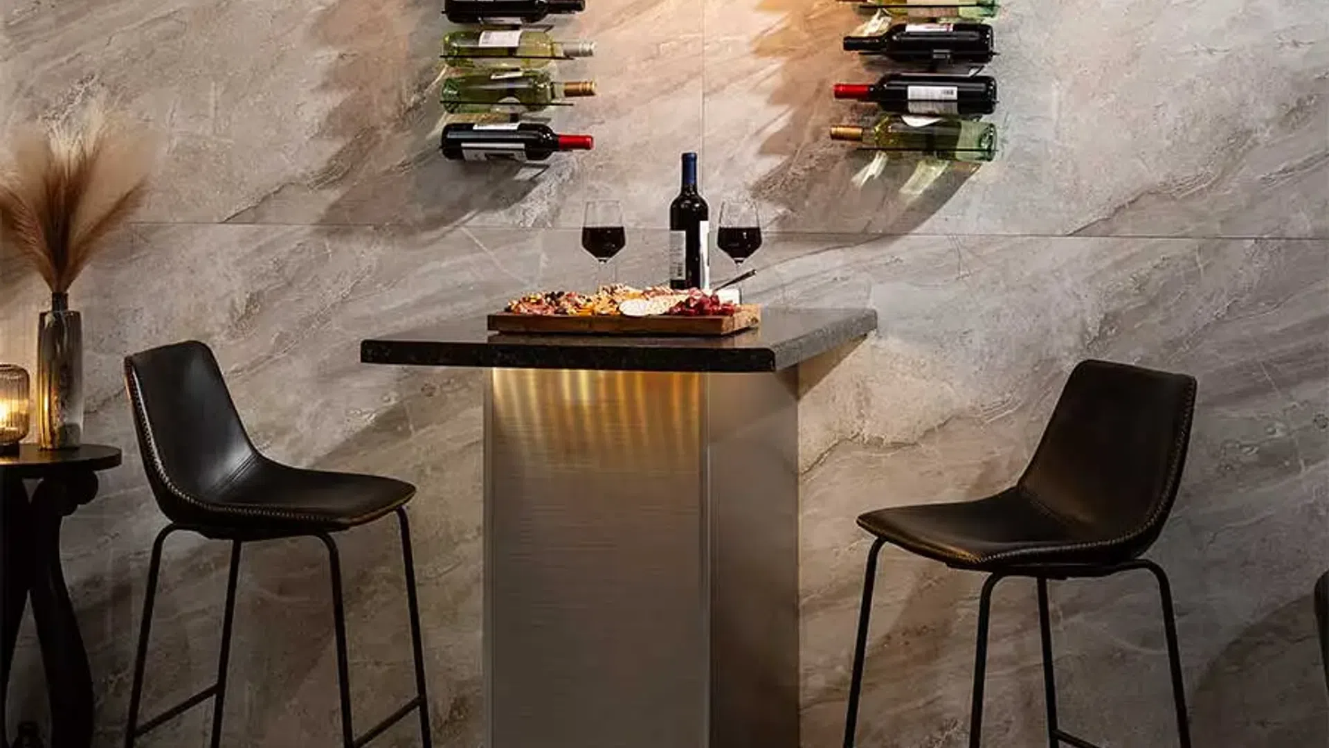 Modern wine tasting setup with two black chairs, wall-mounted wine racks, and illuminated pendant lights.