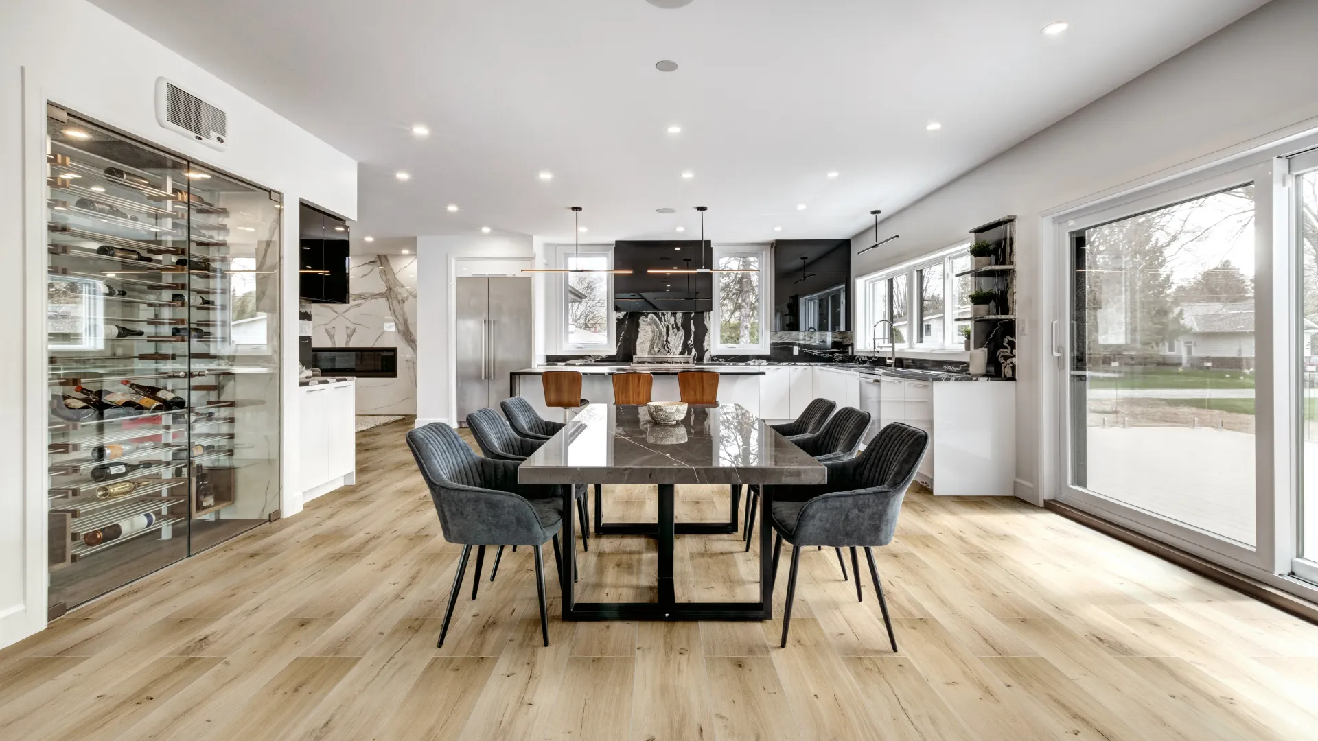 Modern open-concept kitchen and dining area with glass wine fridge, marble island, and large windows.