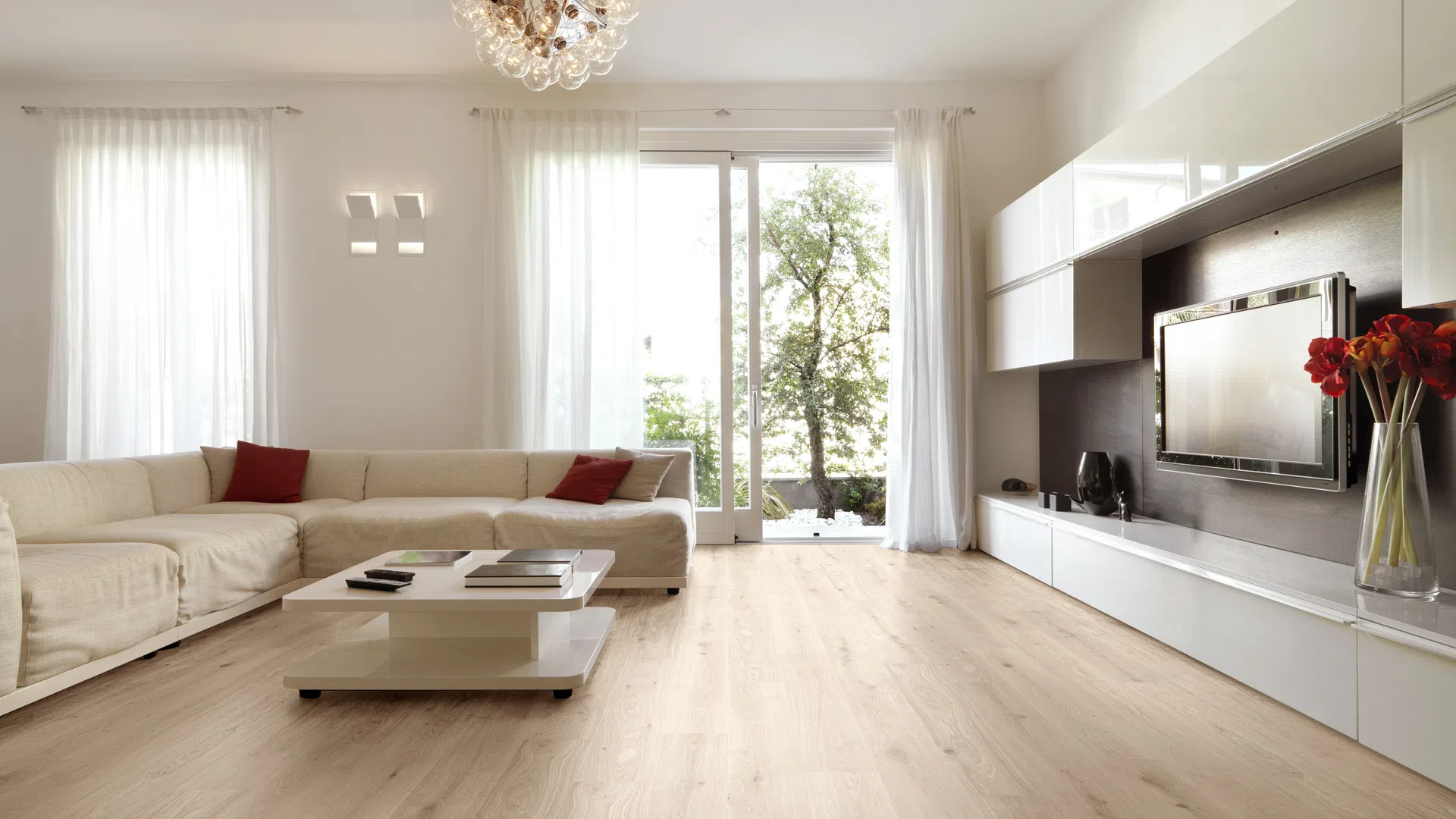 Modern living room with beige sectional sofa, wooden flooring, large window, and white cabinetry with a TV.