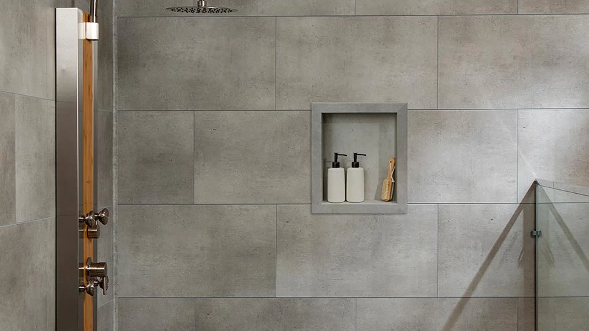 Modern shower with large rain shower head, gray tiled walls, built-in shelf, and bench with folded towels.
