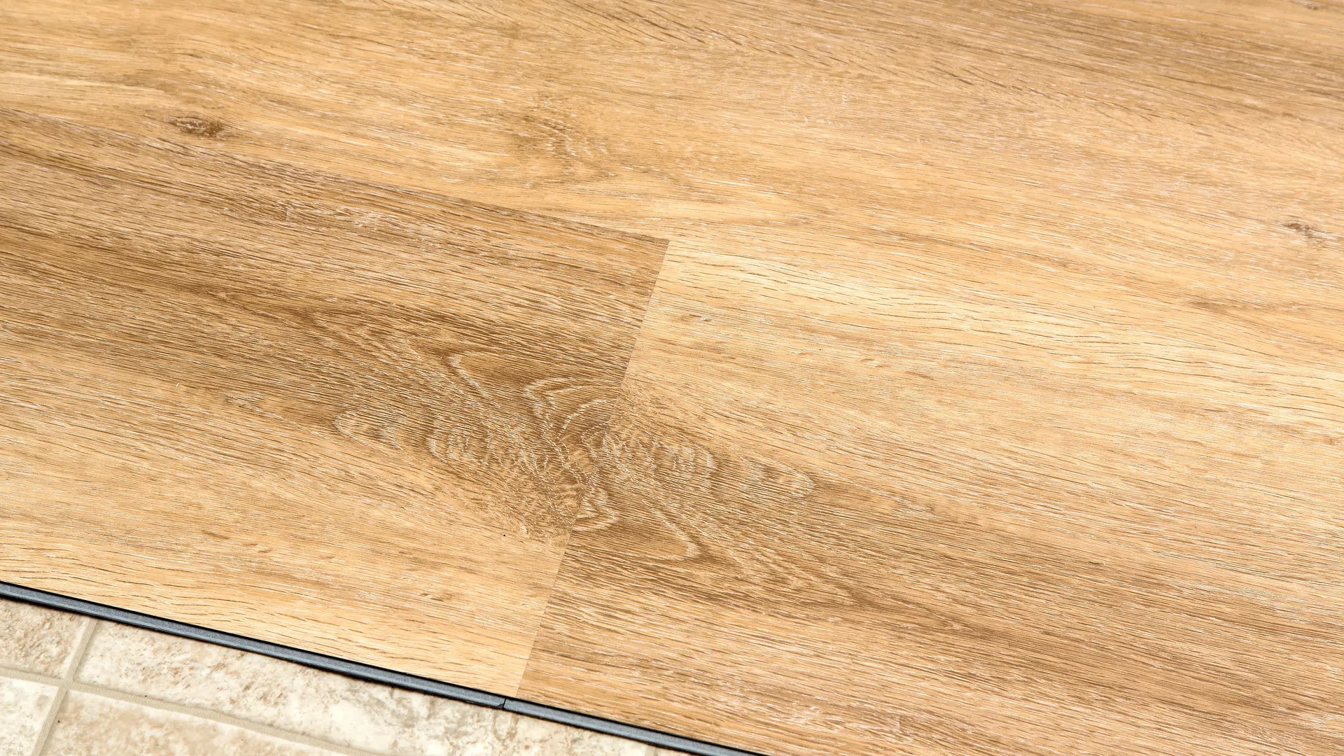 Close-up of beige wood laminate flooring next to beige ceramic tile floor with black transition strip.