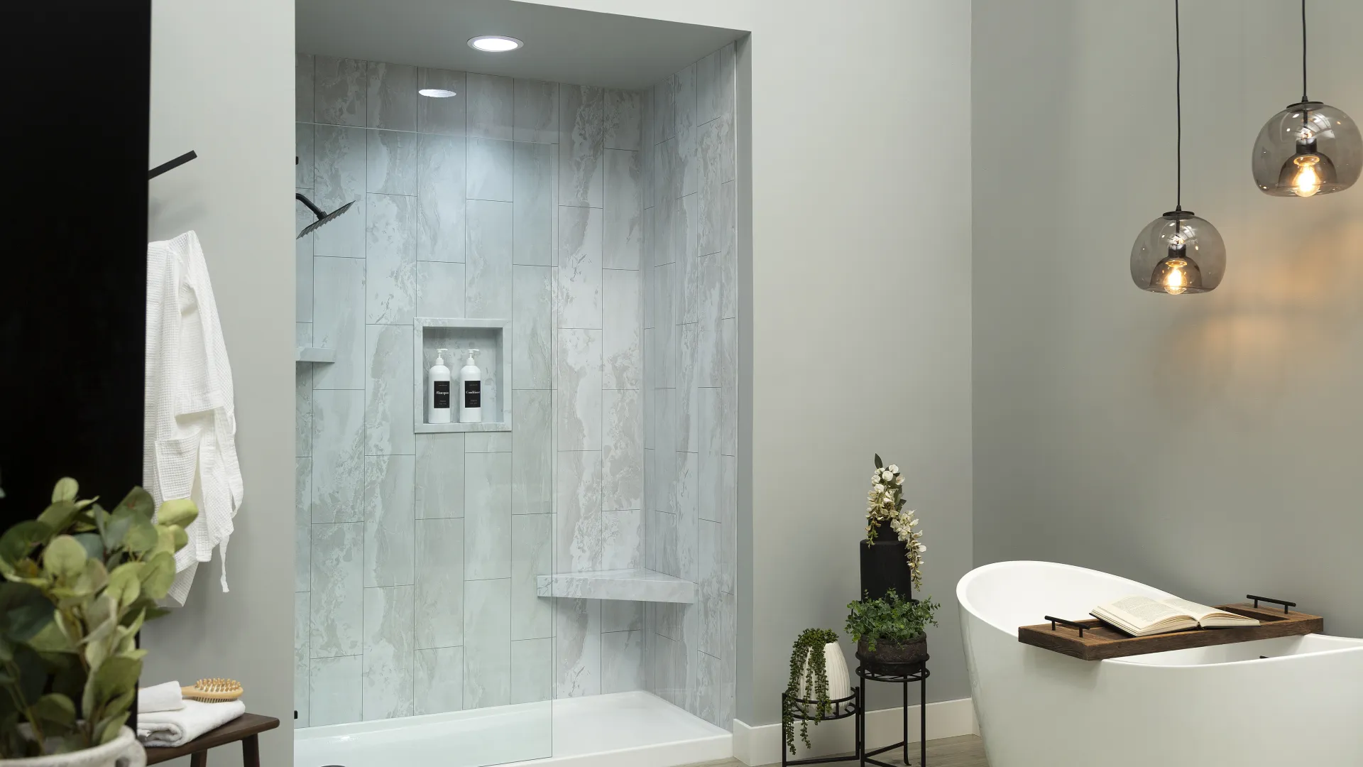 Modern bathroom with marble tiled shower, freestanding bathtub, hanging lights, and decorative plants.