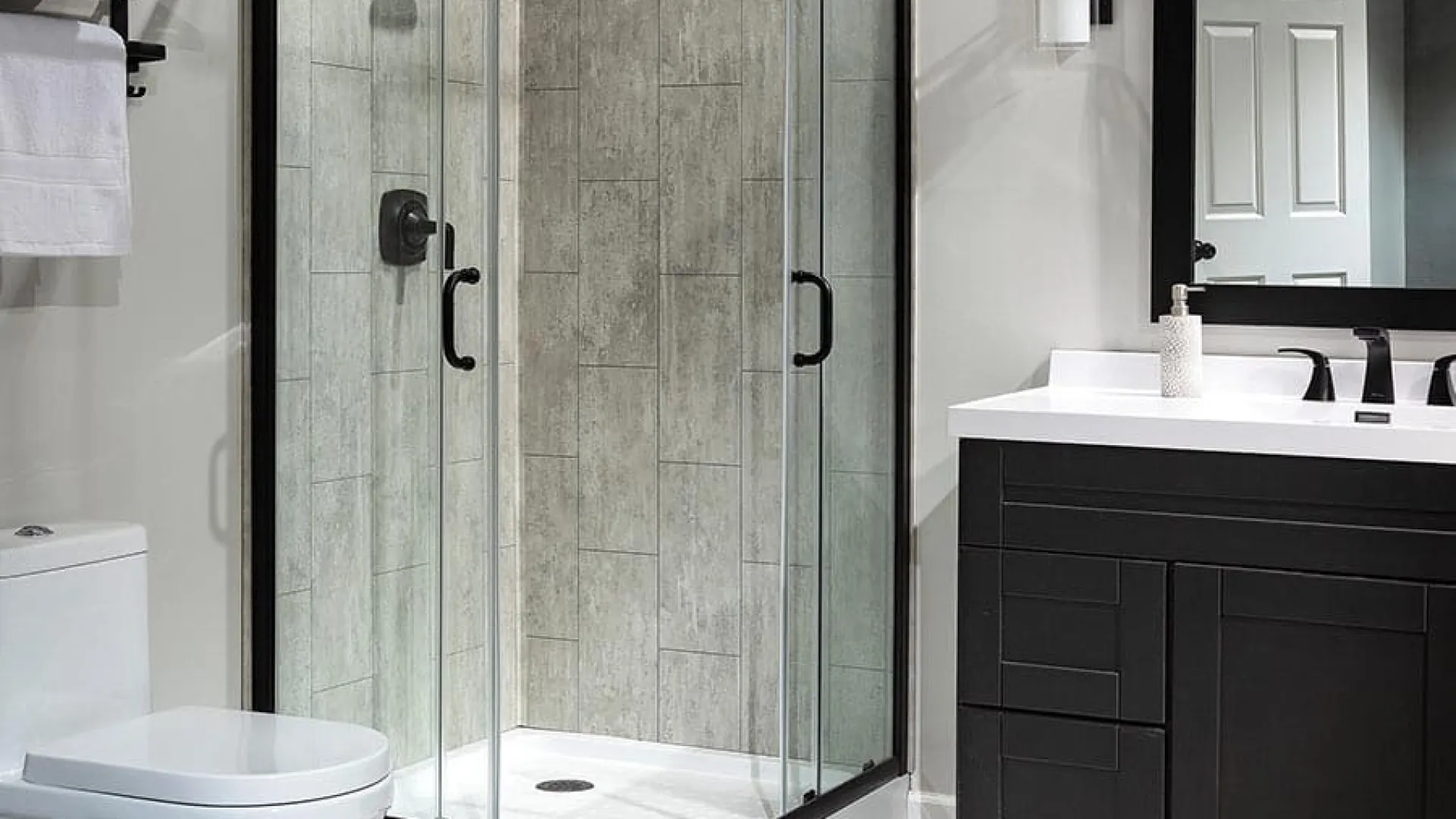 Modern bathroom with glass shower enclosure, black vanity, white toilet, and wall-mounted towel rack