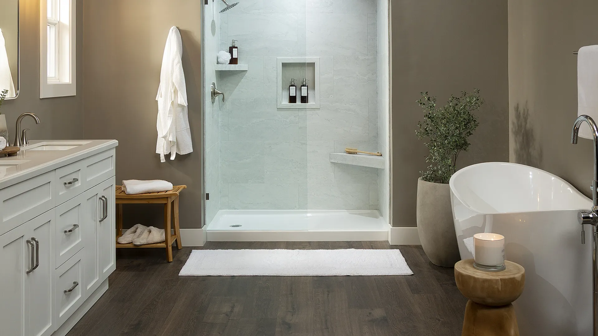 Modern bathroom with glass shower, freestanding tub, wooden floor, white vanity, and neutral walls.