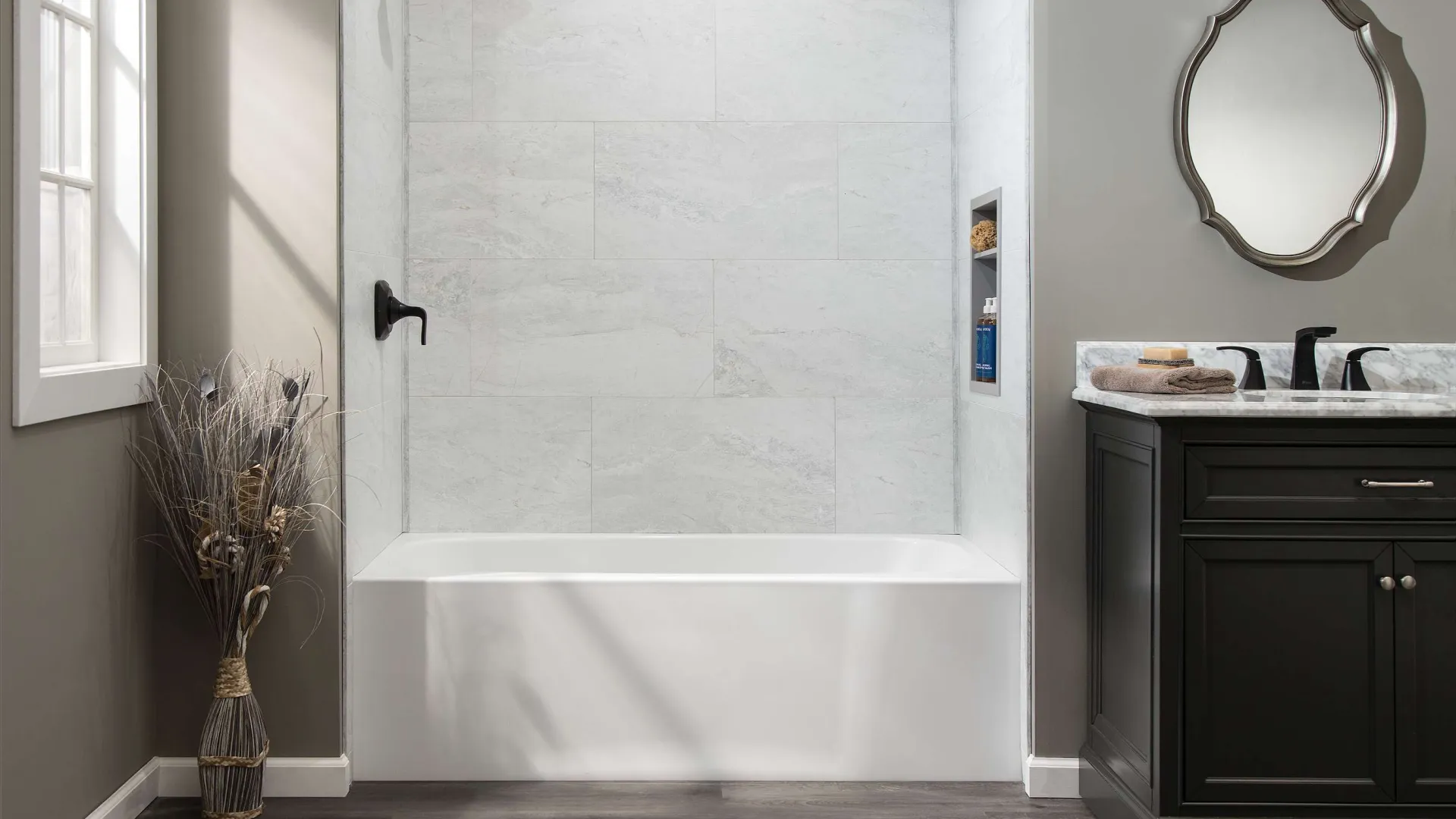 Modern bathroom with white bathtub, dark wood vanity, decorative mirror, and wood-look flooring under natural light.