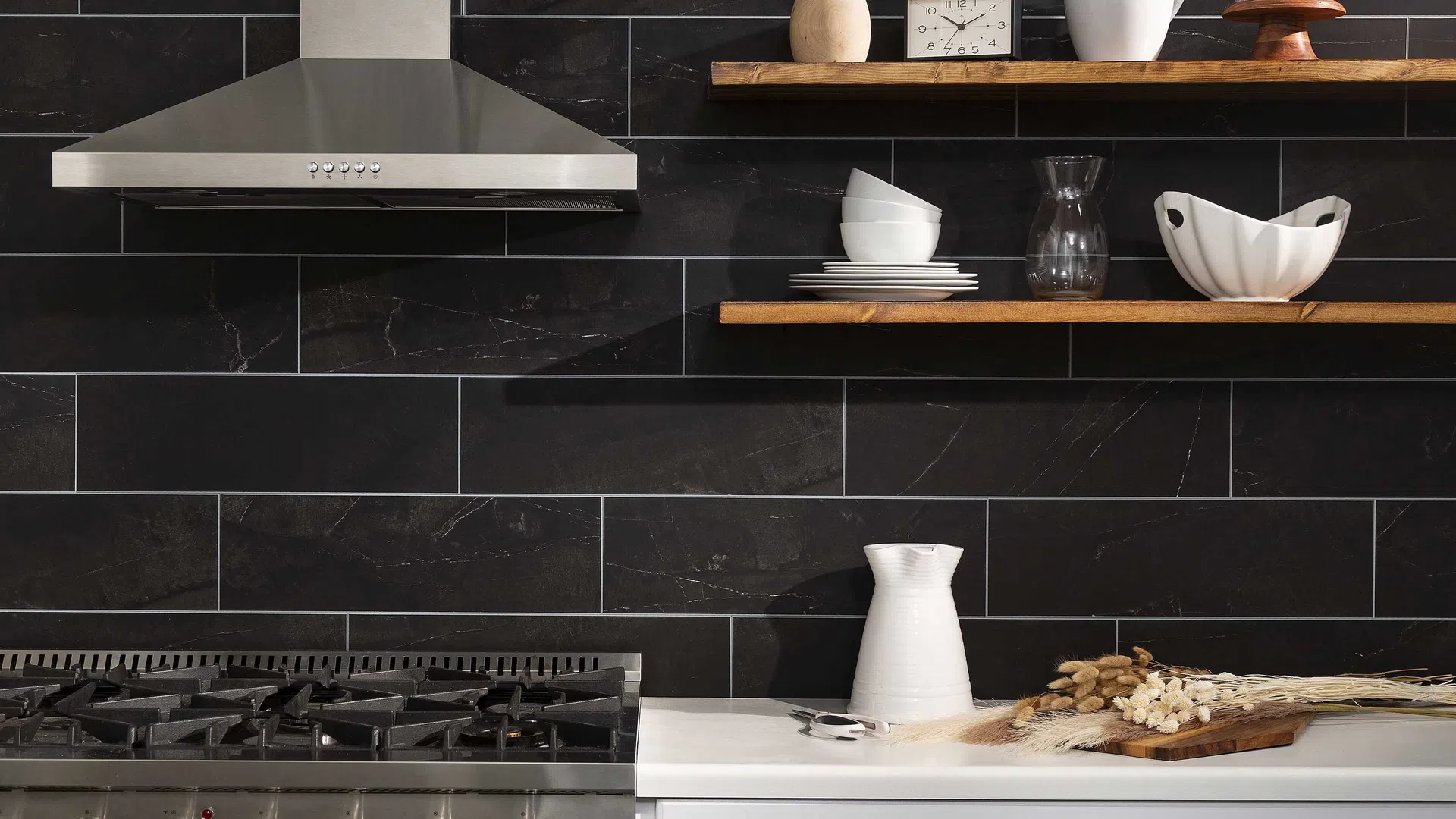 Modern kitchen with stainless steel stove, white cabinets, wood shelves, black tile backsplash, and decorative ceramics.