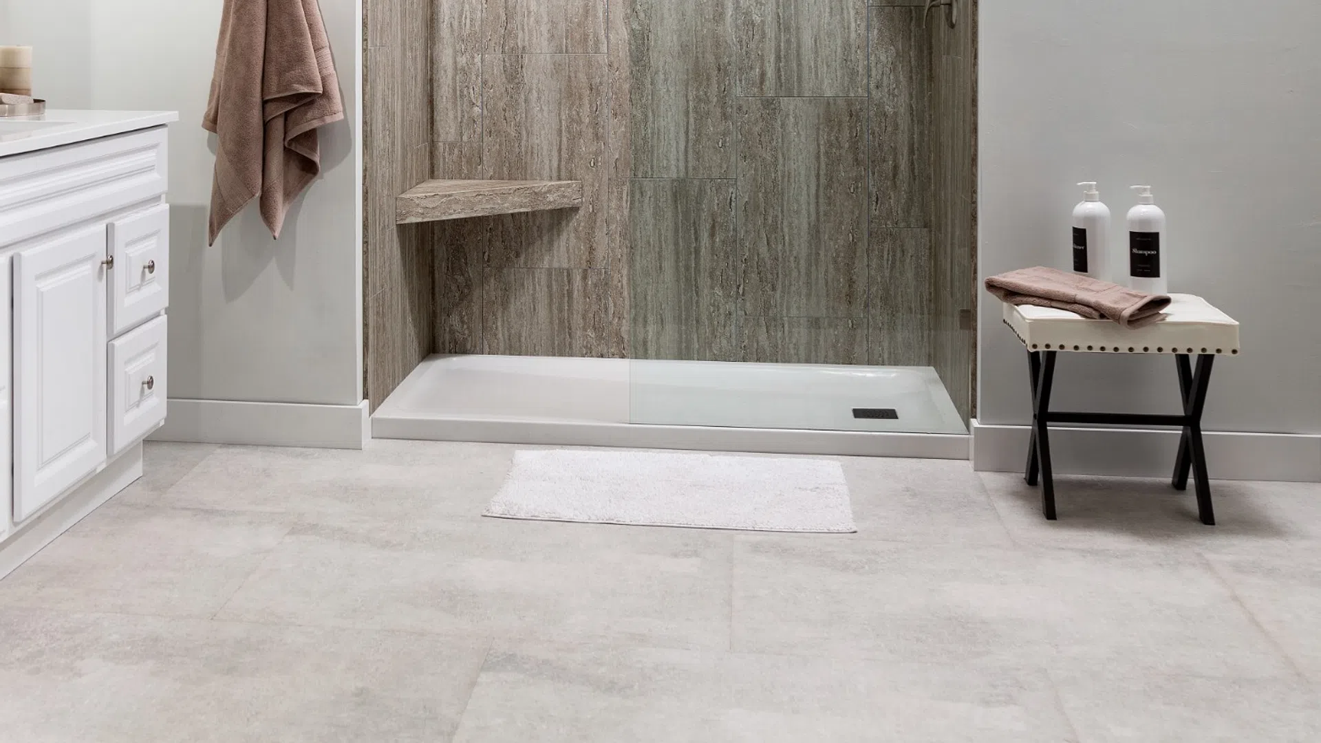 Modern bathroom with walk-in shower featuring stone tile walls, glass panel, towel, and toiletries.