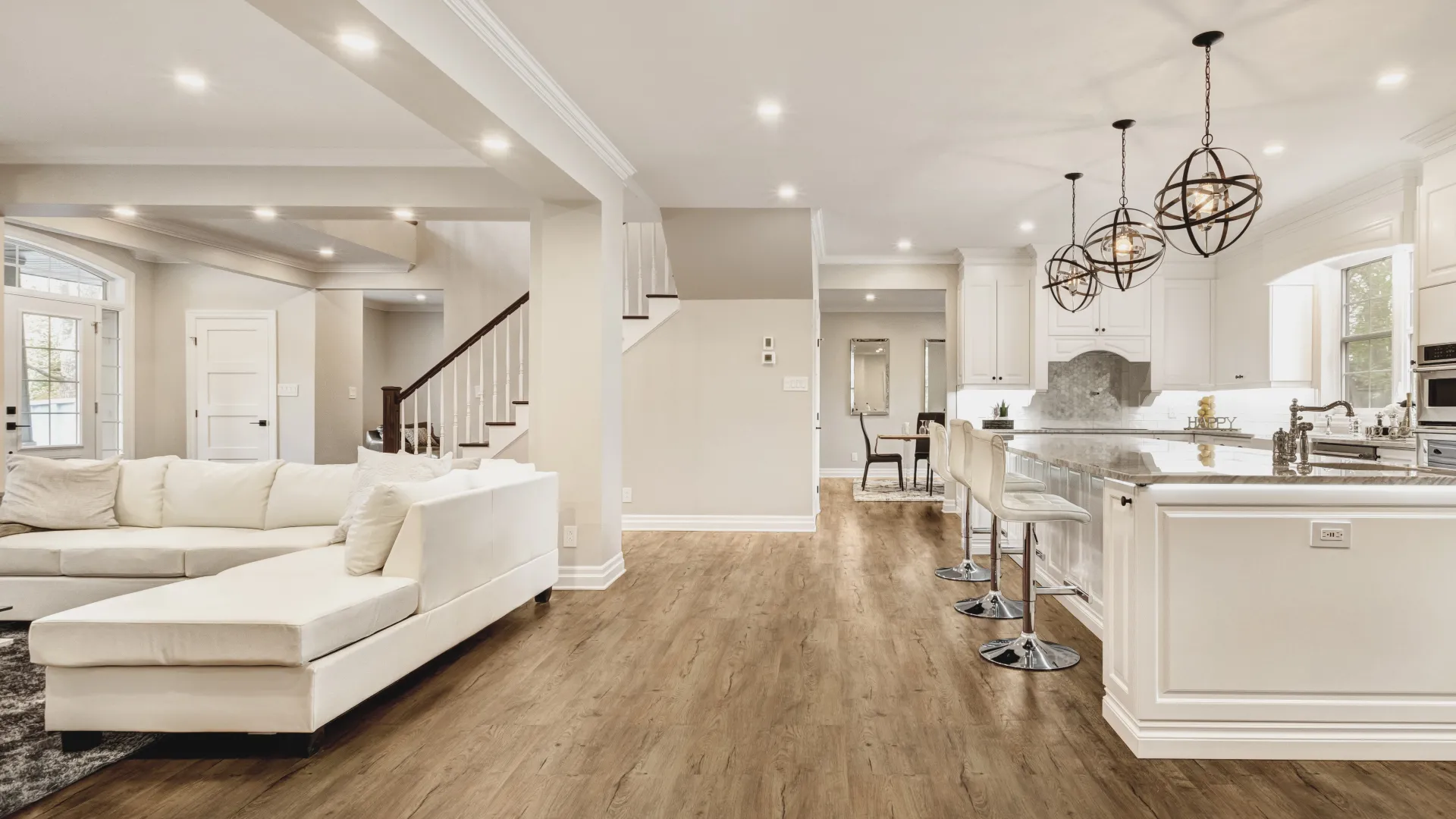 Spacious open-concept living area with white sectional sofa, wood floors, modern kitchen island, and globe pendant lights