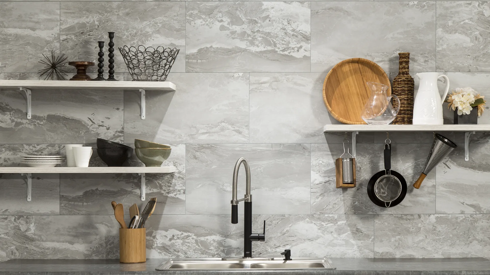 Modern kitchen with gray marble tile backsplash, stainless steel sink, wooden utensils, and open shelves with decor.