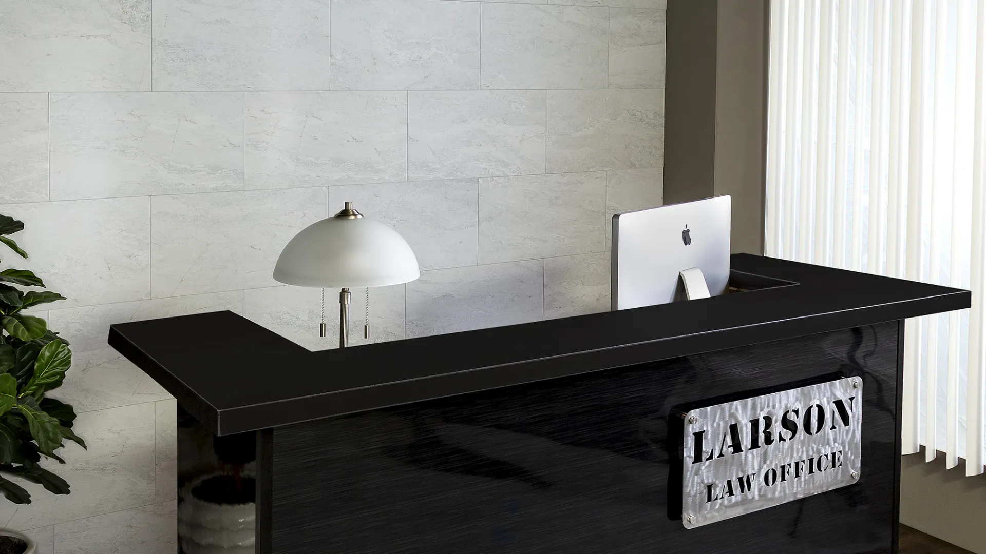 Modern law office reception with black desk, Larson Law Office sign, desk lamp, computer, and window blinds.