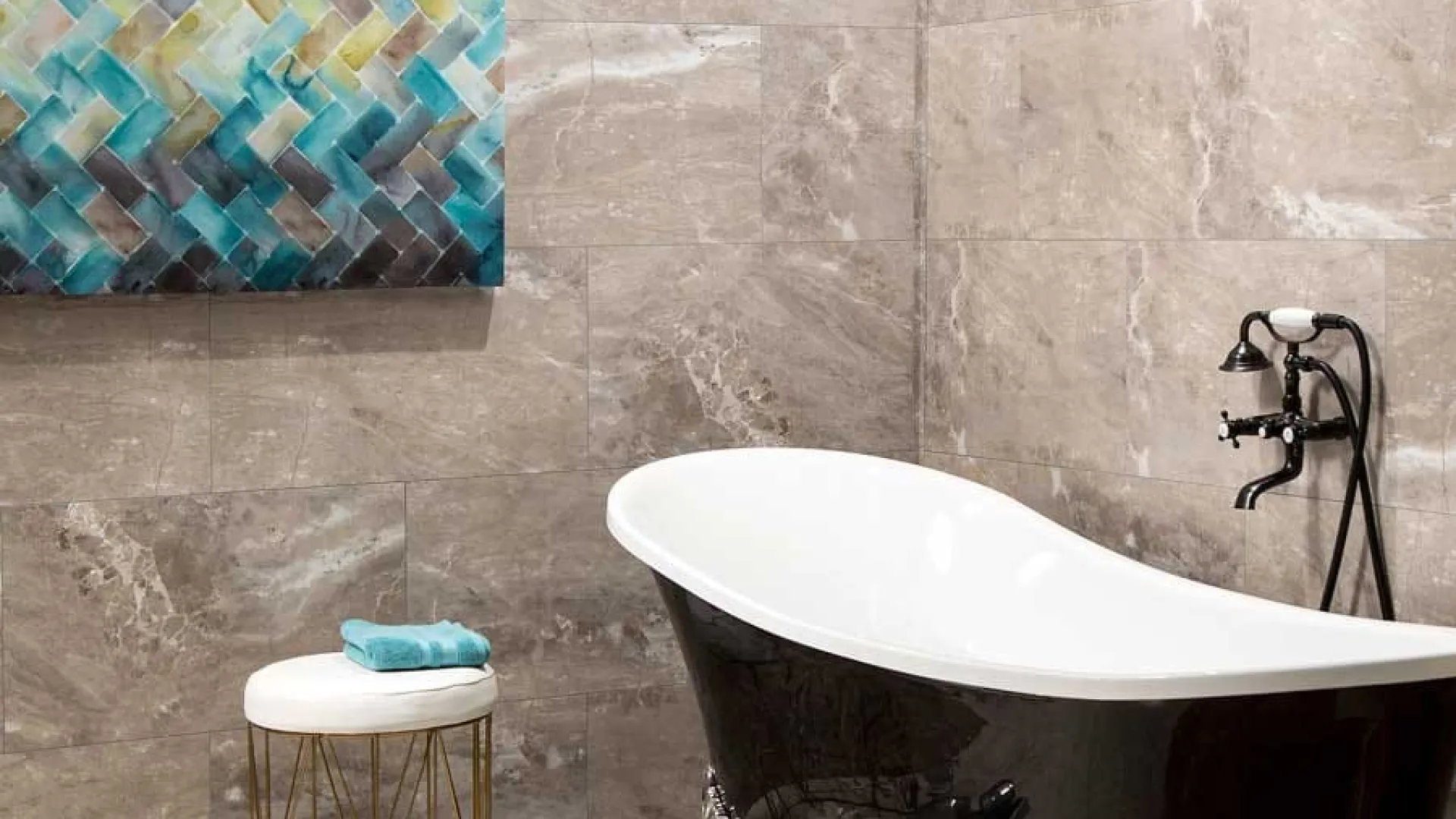 Black clawfoot bathtub with ornate silver feet in a modern bathroom with gray tile walls and abstract artwork.
