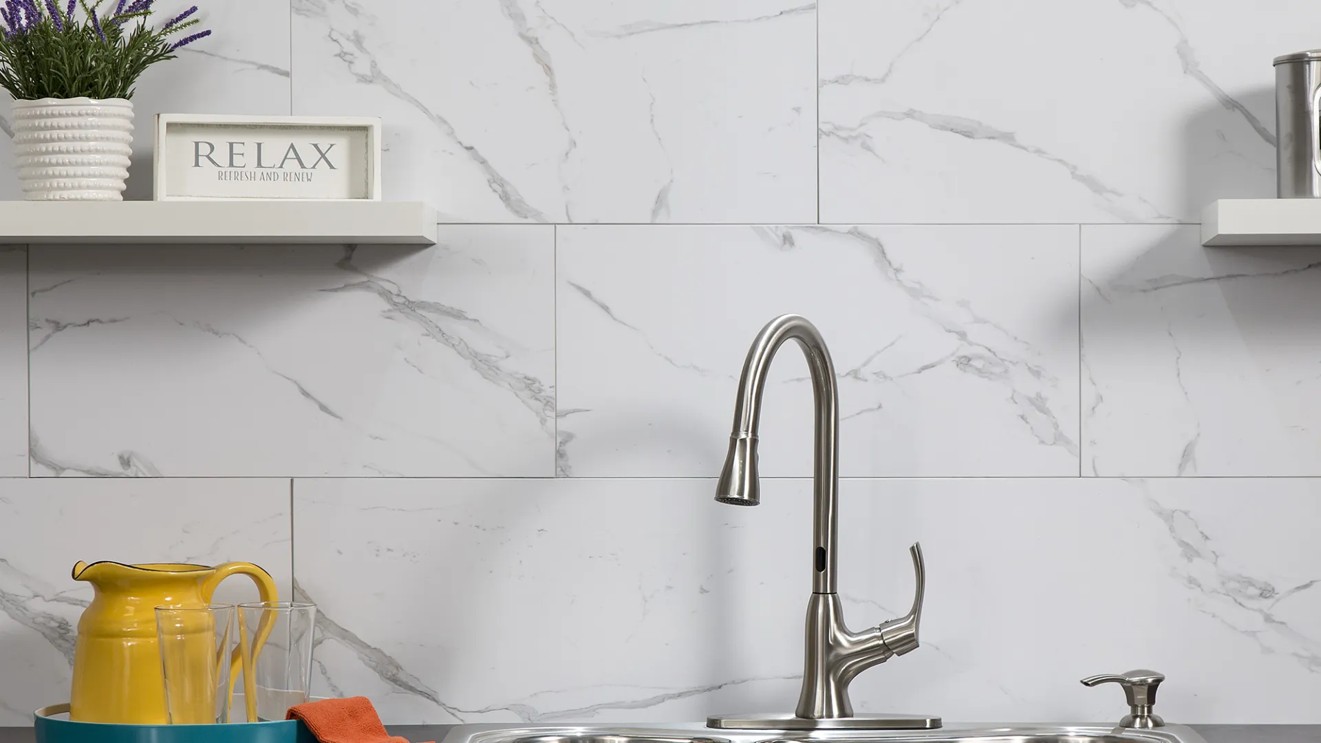 Modern kitchen sink with stainless steel faucet, white marble backsplash, and accessories on black countertop.