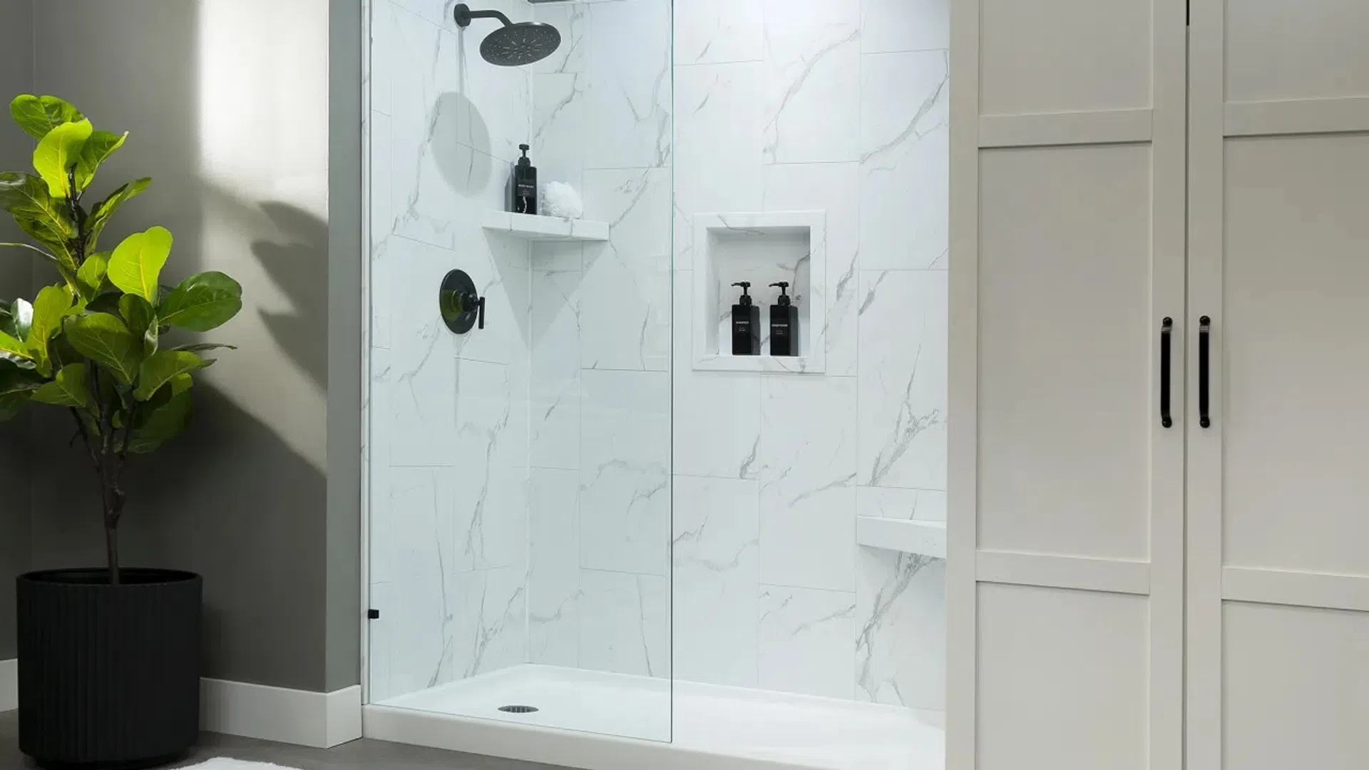 Modern white marble bathroom shower with rain showerhead and built-in shelves beside a large potted plant.