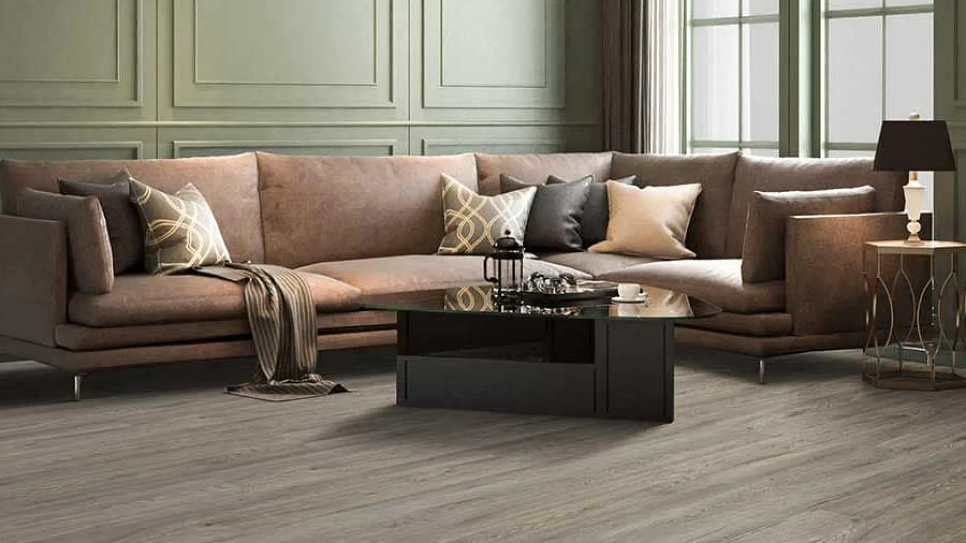Modern living room with brown sectional sofa, glass coffee table, green paneled walls, and large windows.