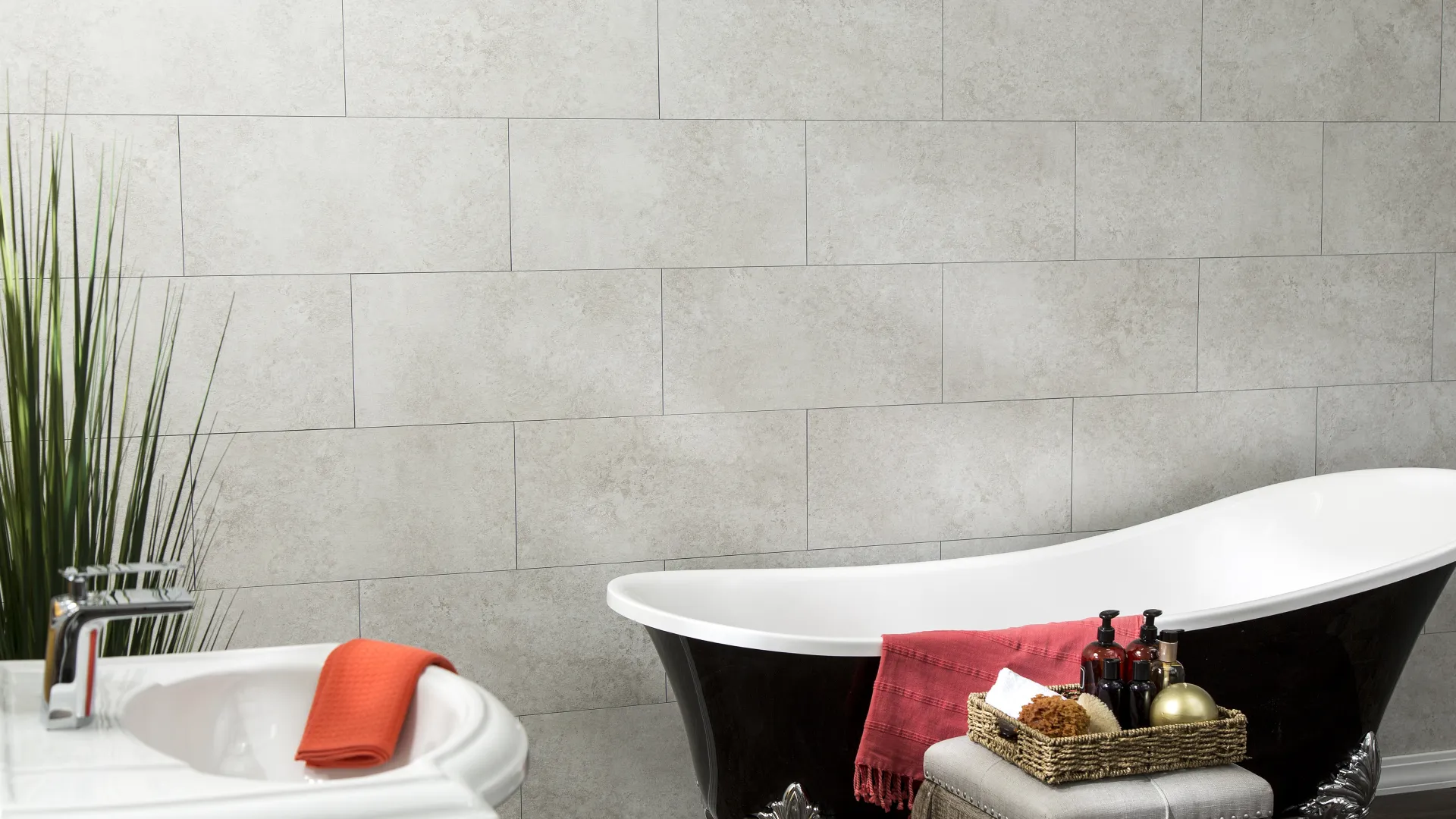 Elegant black clawfoot bathtub with red towel and basket of toiletries in modern bathroom with stone tiles.