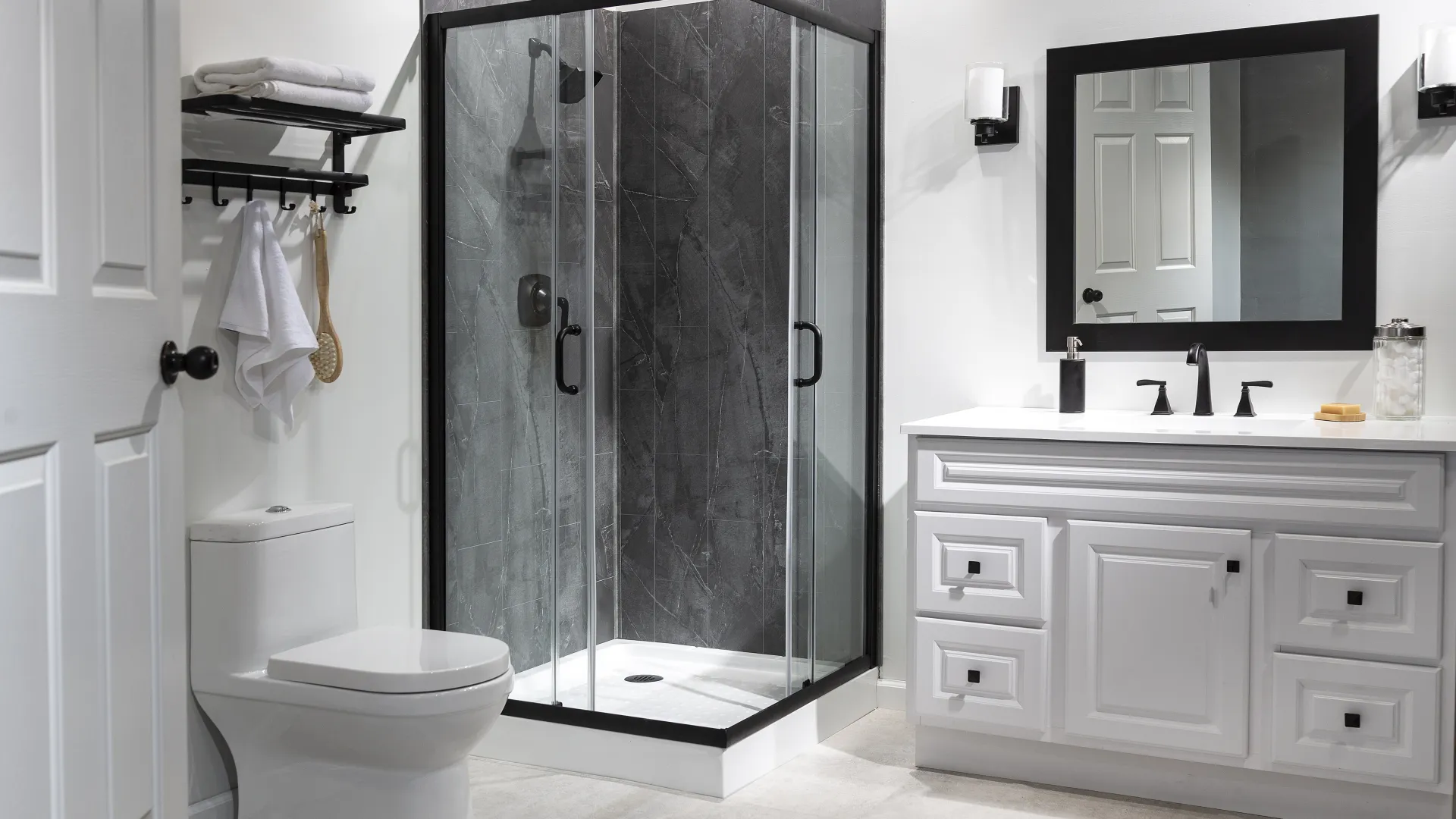 Modern bathroom with glass shower, white vanity, black fixtures, toilet, mirror, and towel rack.