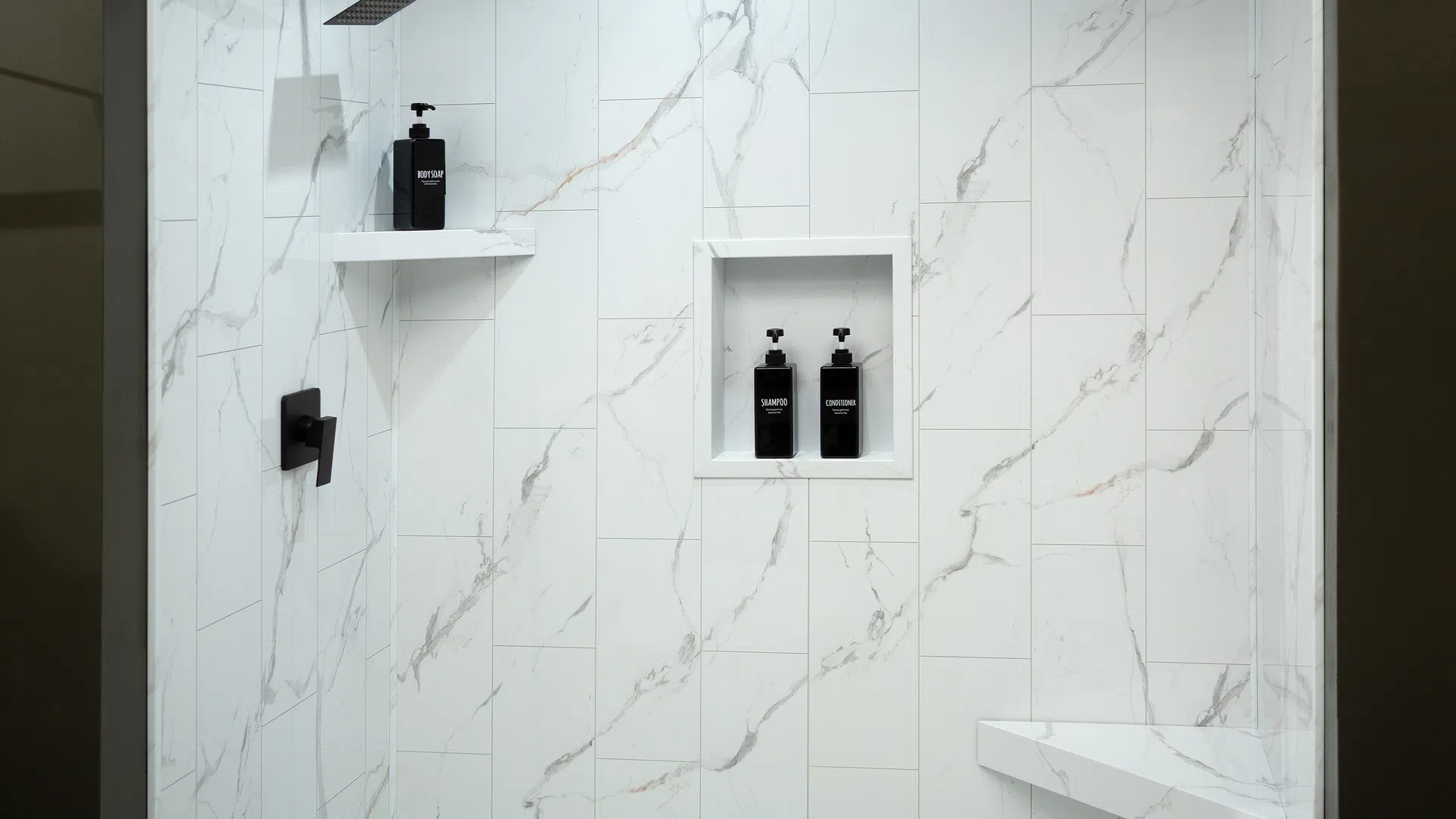 Modern shower with white marble tiles, black shower fixtures, built-in shelves, and black soap dispensers