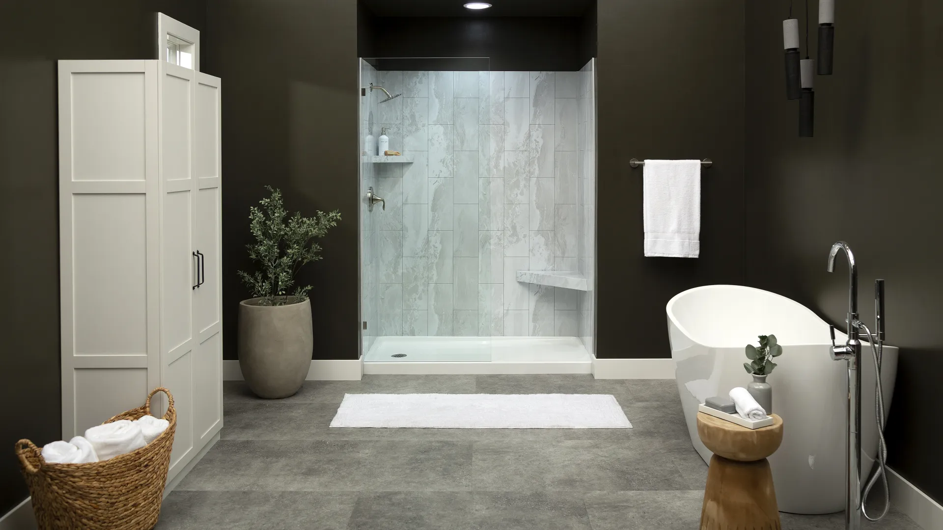 Modern bathroom with glass shower, freestanding bathtub, white towels, large plant, and dark walls.