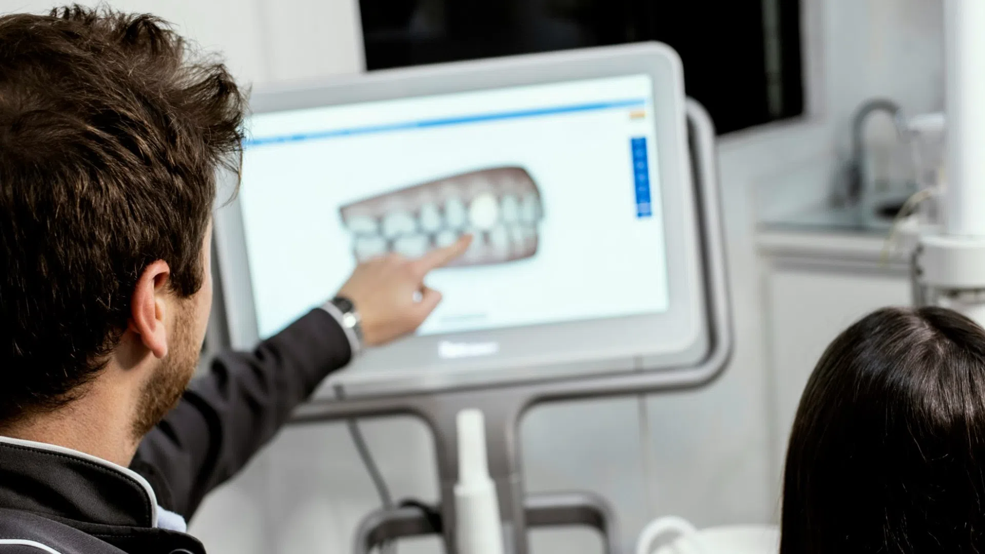 Dentist explaining dental X-ray on screen to patient sitting in dental chair during consultation.