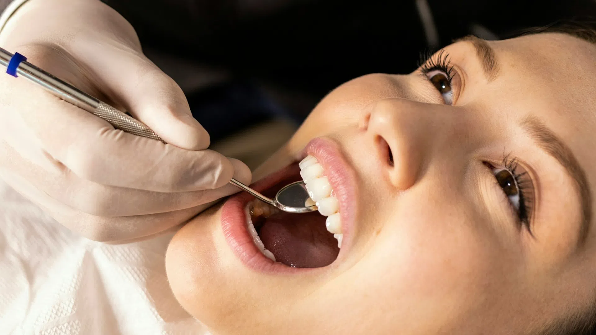 Orthodontist in gloves examining young woman's teeth with dental mirror during checkup.