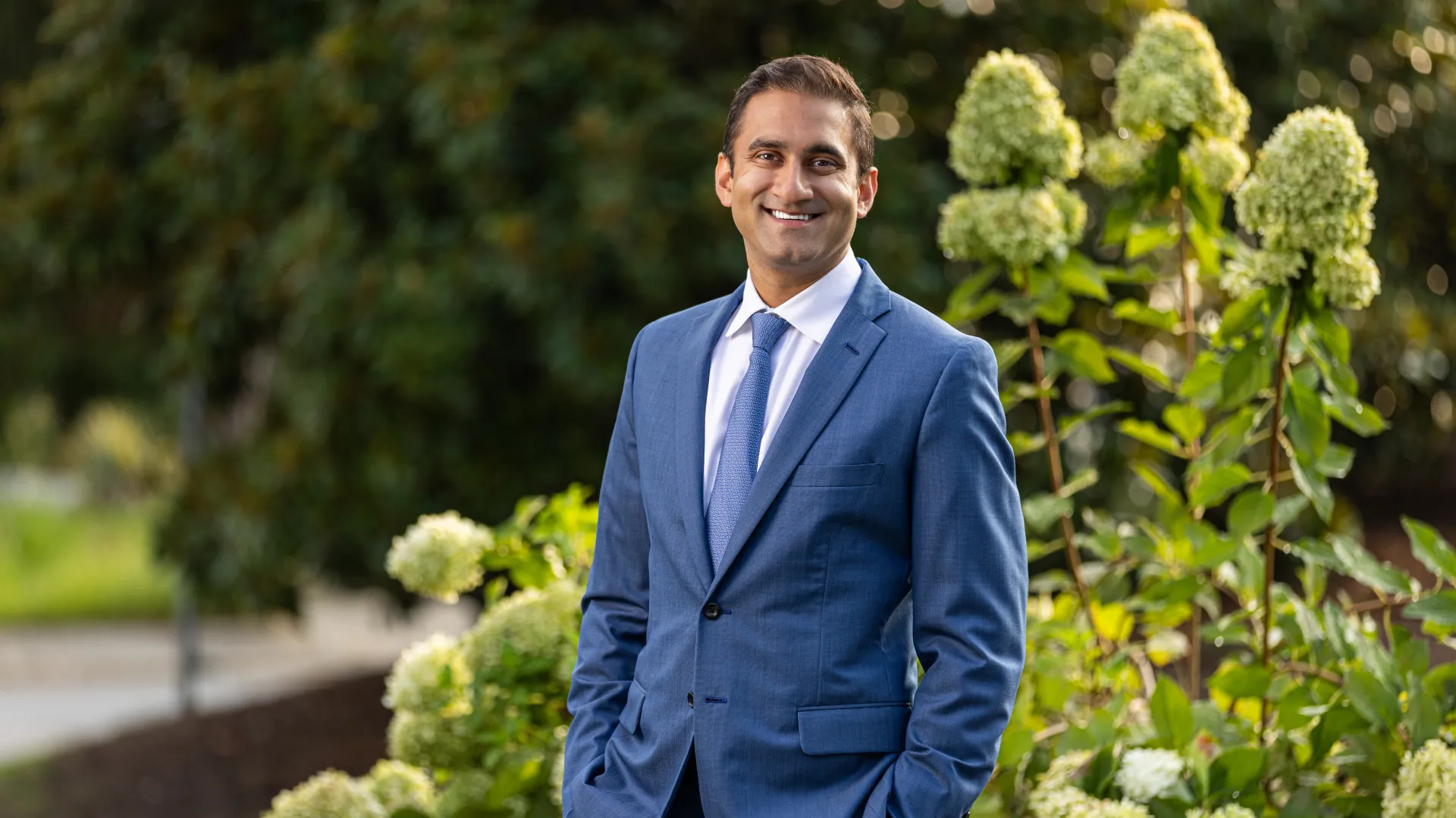 a man in a suit standing in front of a bush