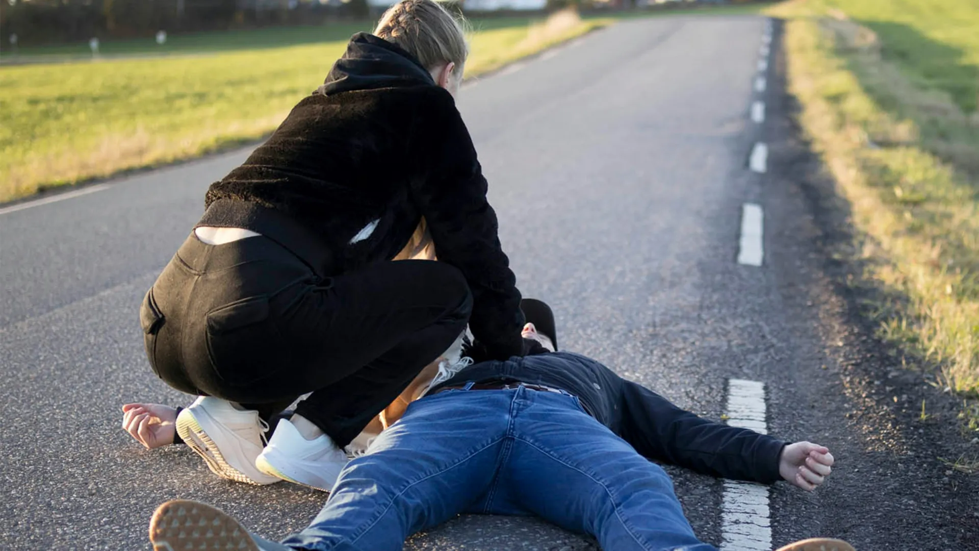 a man kneeling on the side of a road with another man kneeling on the ground