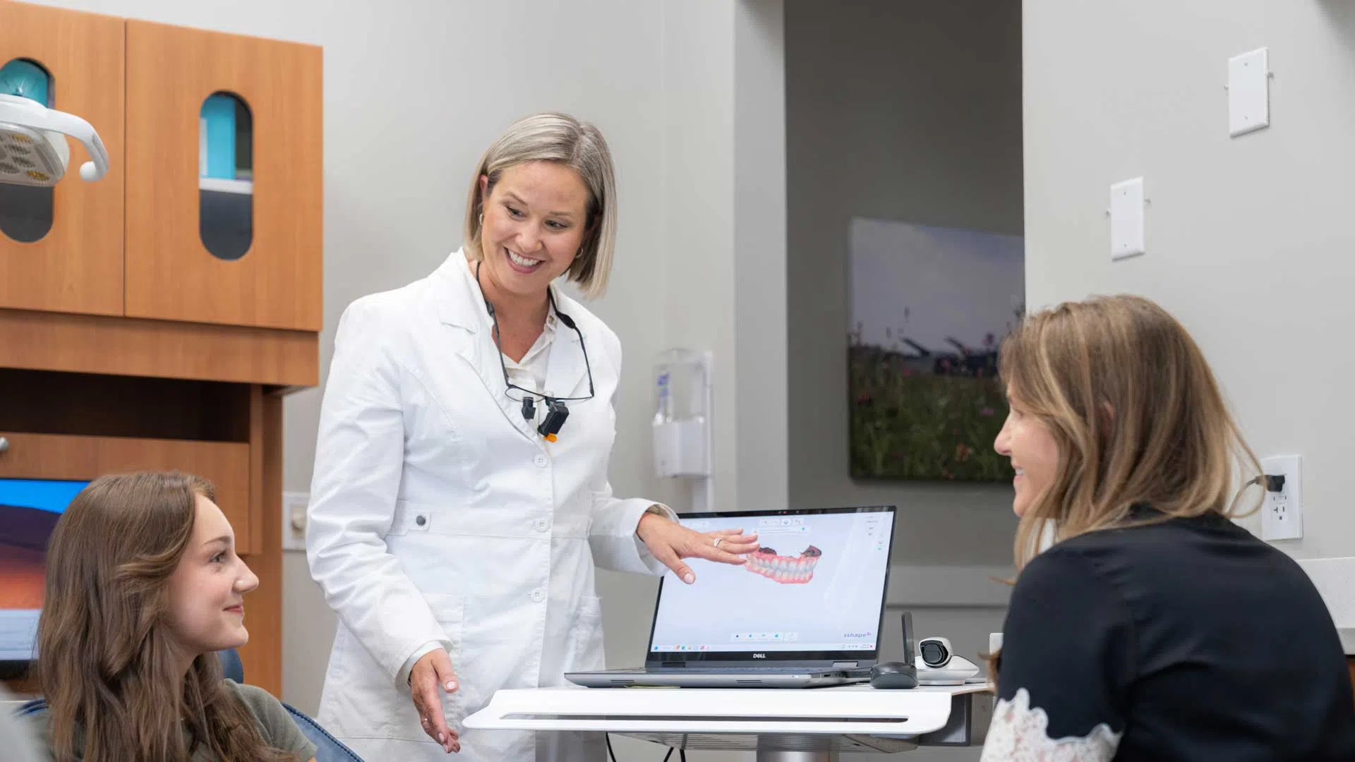 Dental professional explaining digital teeth scan results to two female patients in a modern clinic.