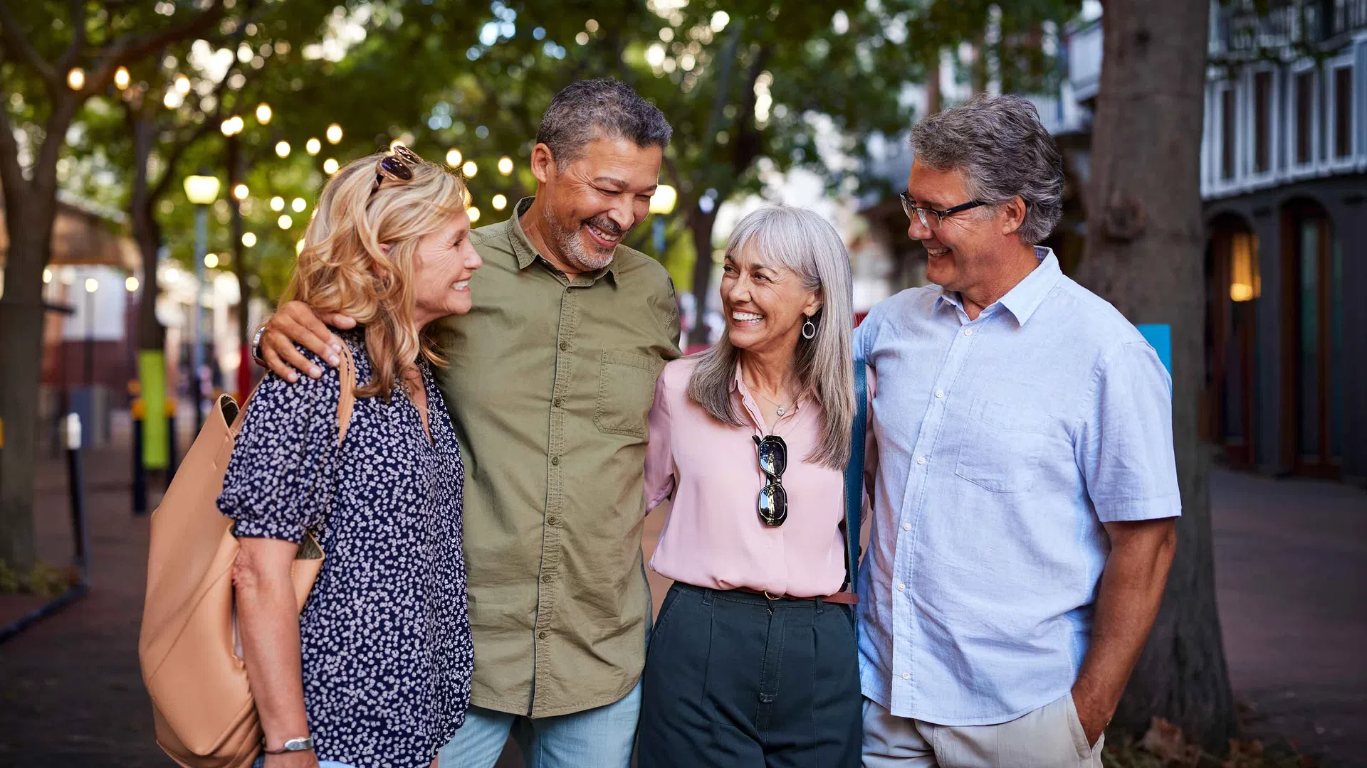 Happy mature friends smiling and walking together outdoors on a tree-lined street in casual attire.