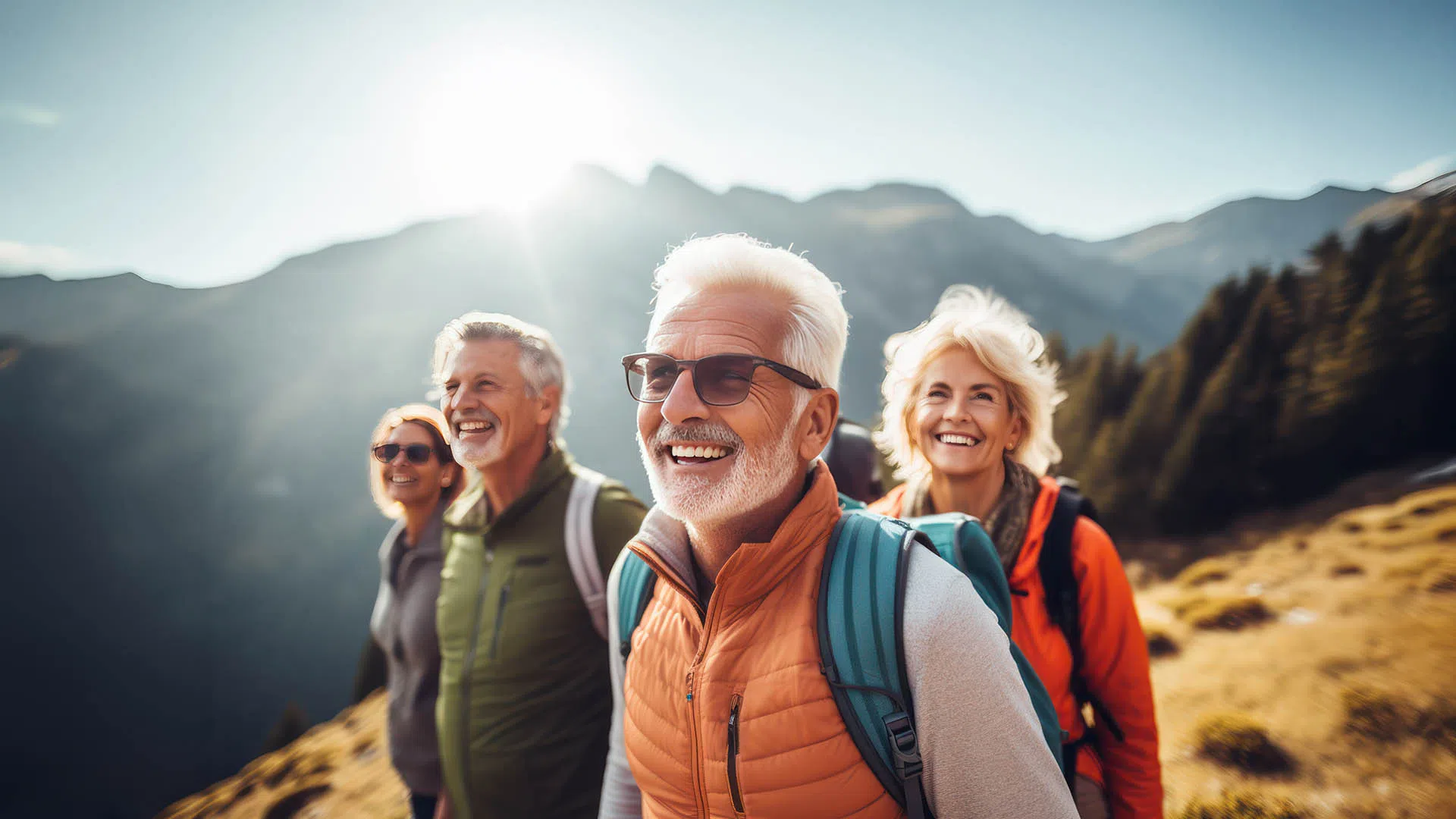 Happy senior friends hiking in mountains under bright sun with backpacks and casual outdoor clothing.