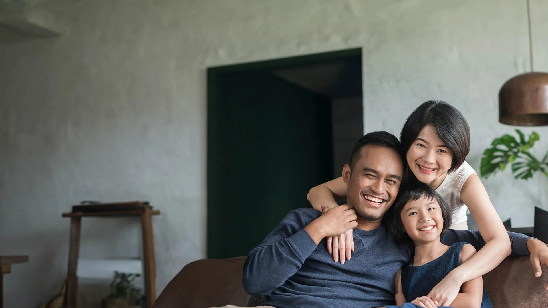 Happy family of three smiling and hugging on a sofa in a cozy modern living room
