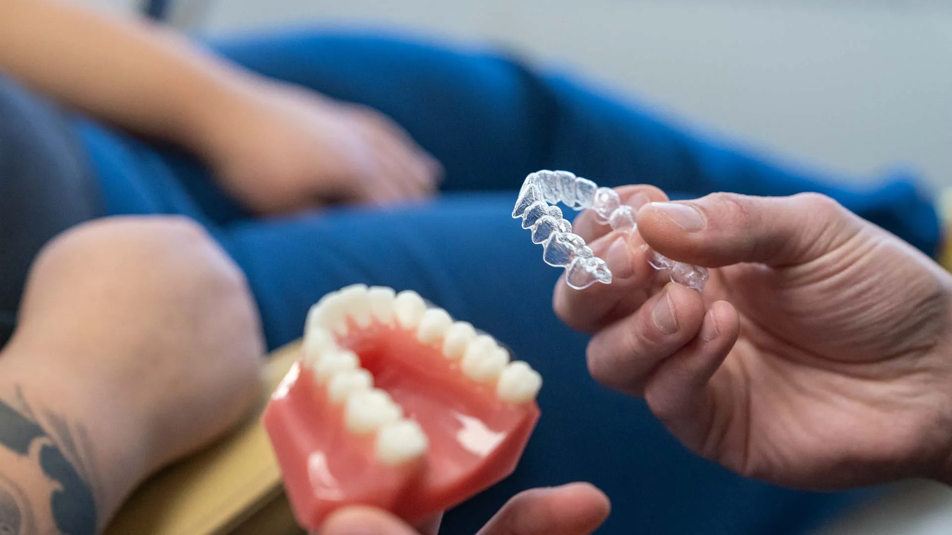 Close-up of hands holding dental model and clear aligner for orthodontic teeth straightening.