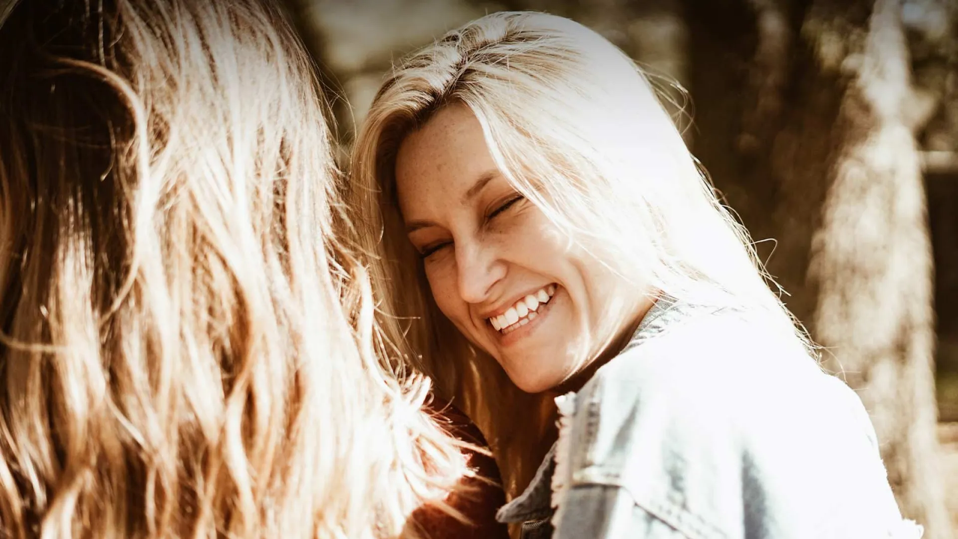 Two young women laughing together outdoors, exuding friendship and joy amidst nature.