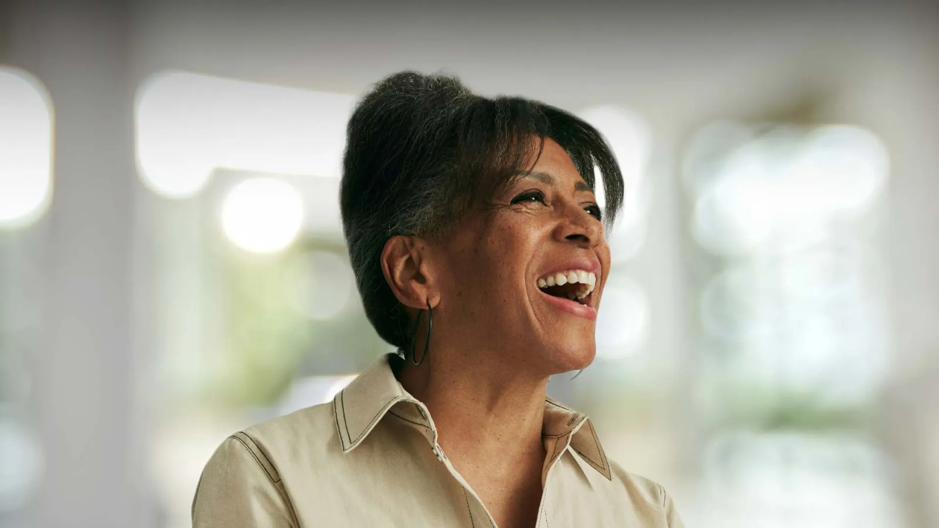 Smiling woman in a light-colored shirt, with a soft blurred background, conveying joy and positivity.