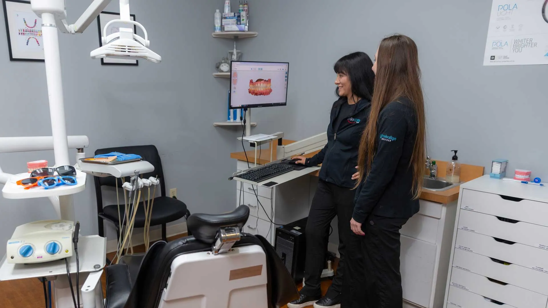Two dental professionals review 3D dental imaging on a computer in a modern dental exam room.