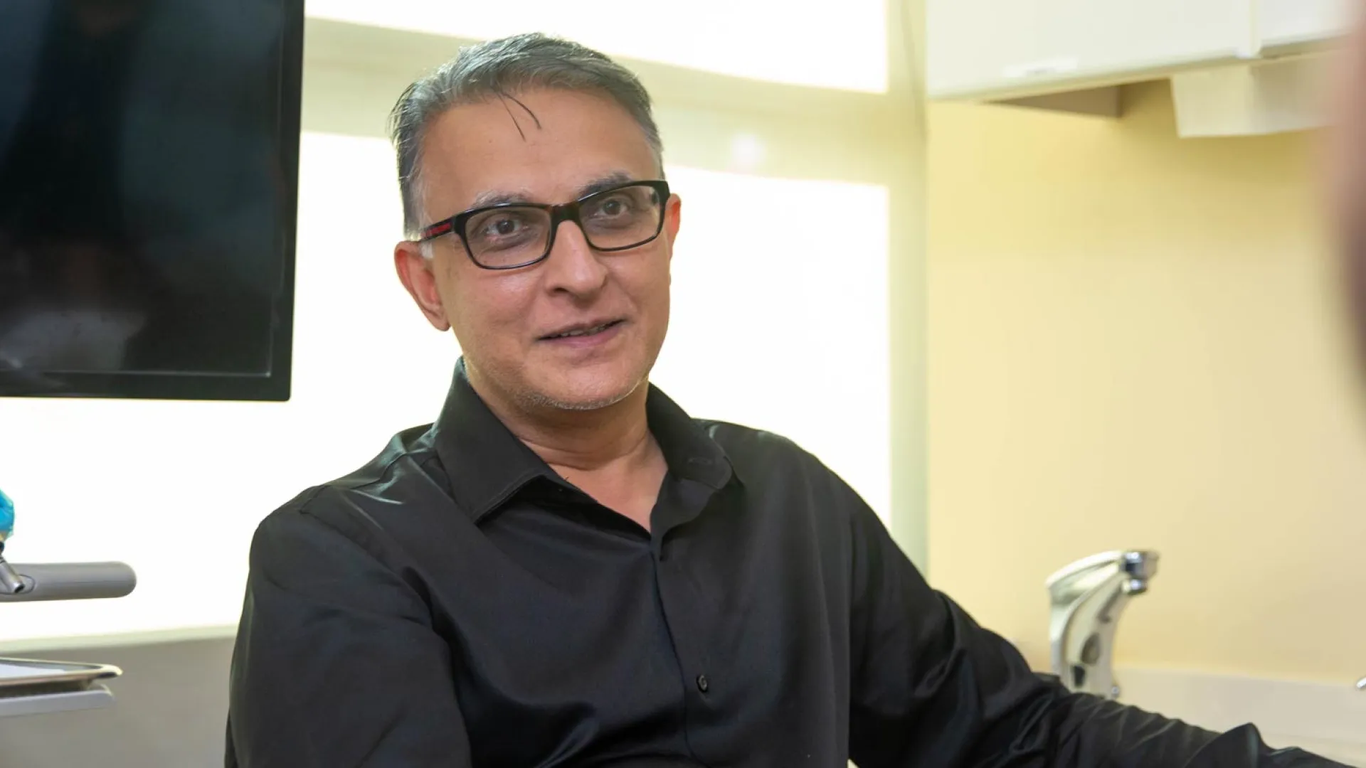 A professional man in a black shirt engages in conversation at a modern office setting.