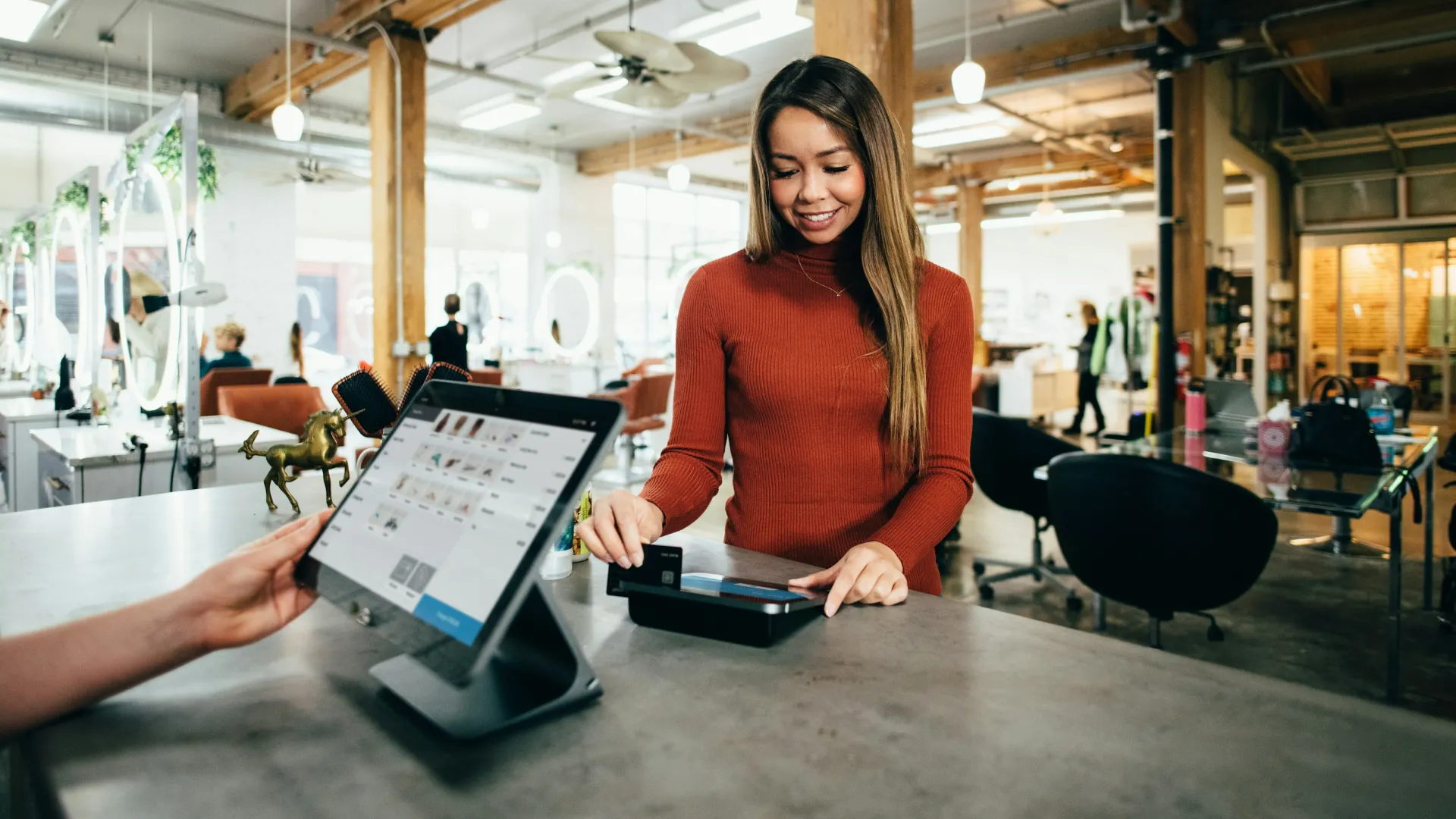 Young woman making a payment with a credit card at a modern retail store counter with a touchscreen register.